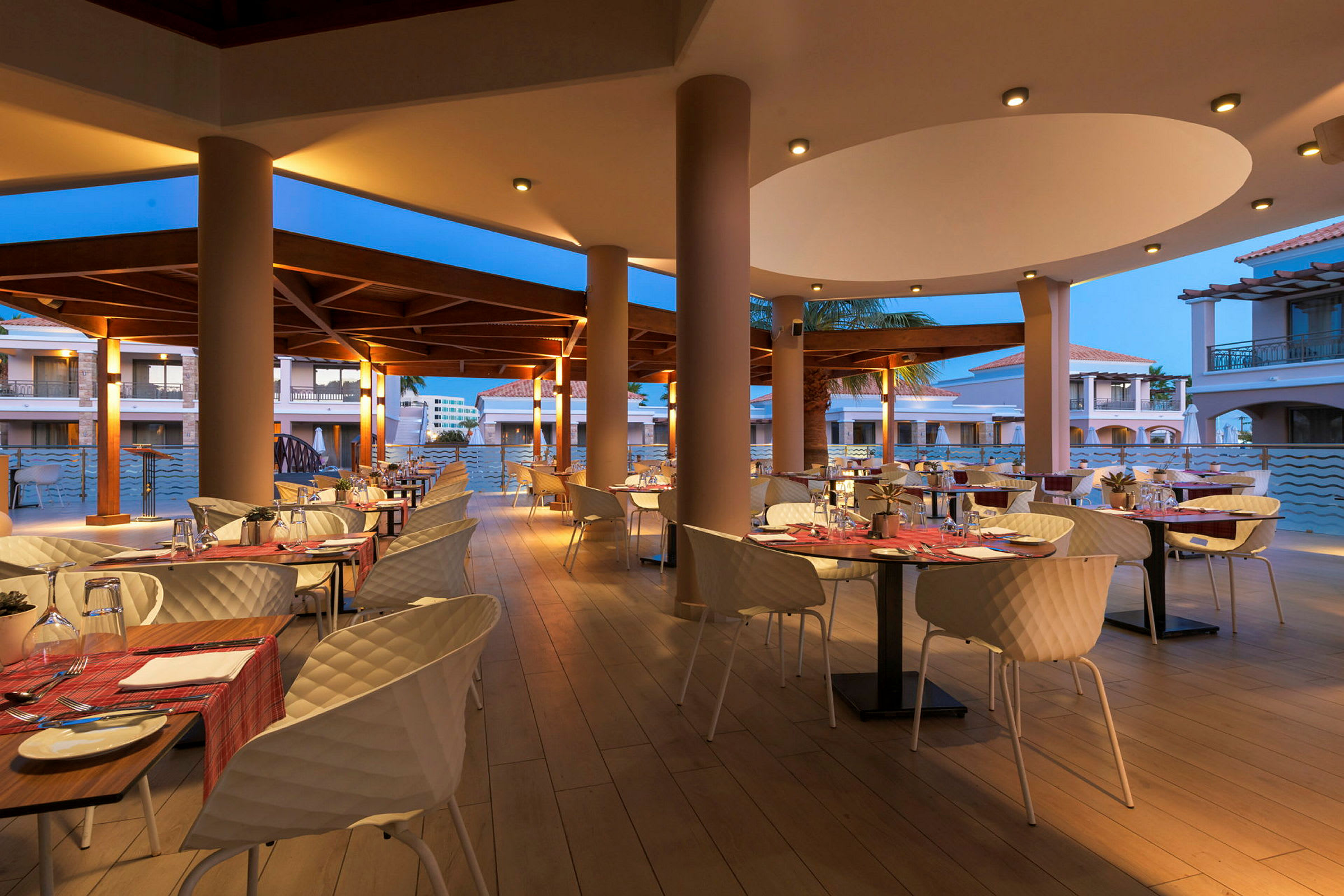 Spiseområde med bord og stoler utendørs på en restaurant med kveldsbelysning. (AI-generert tekst)