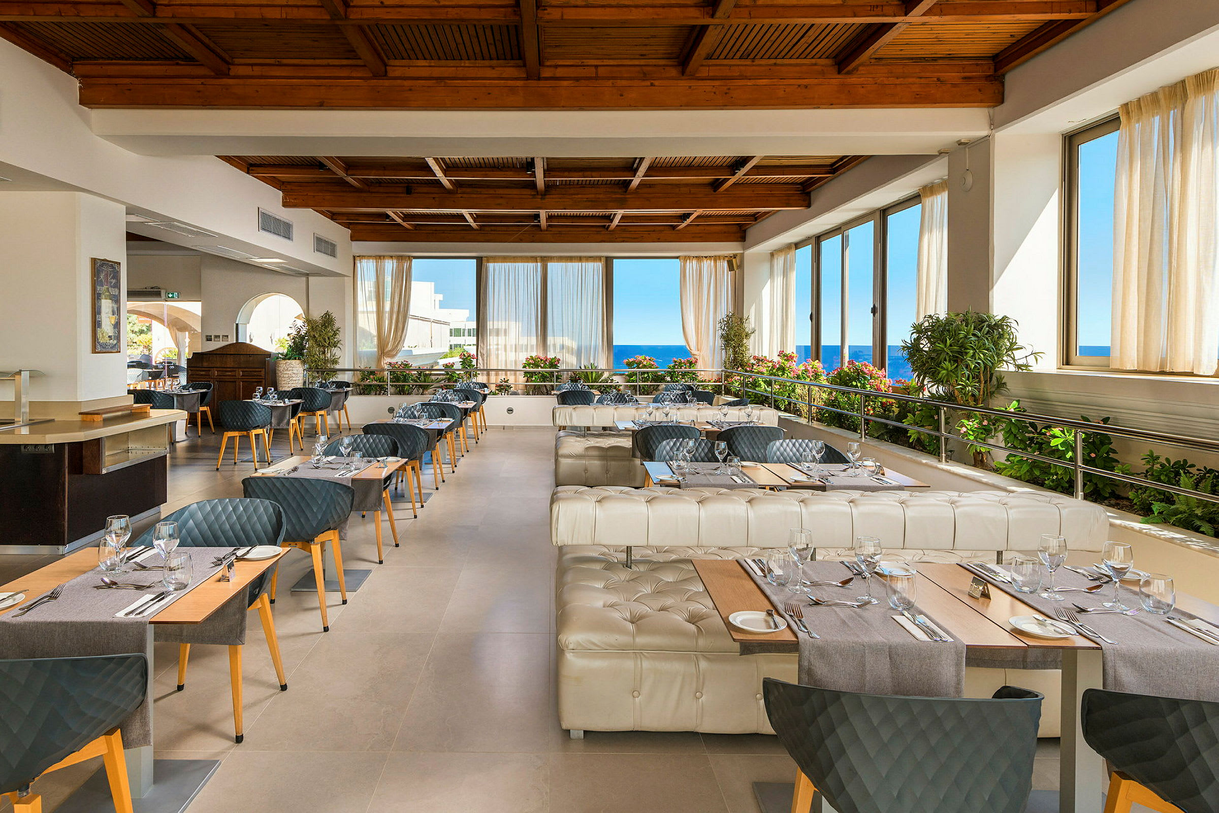 Restaurant med bord, stoler og vinduer med utsikt mot havet. (AI-generert tekst)