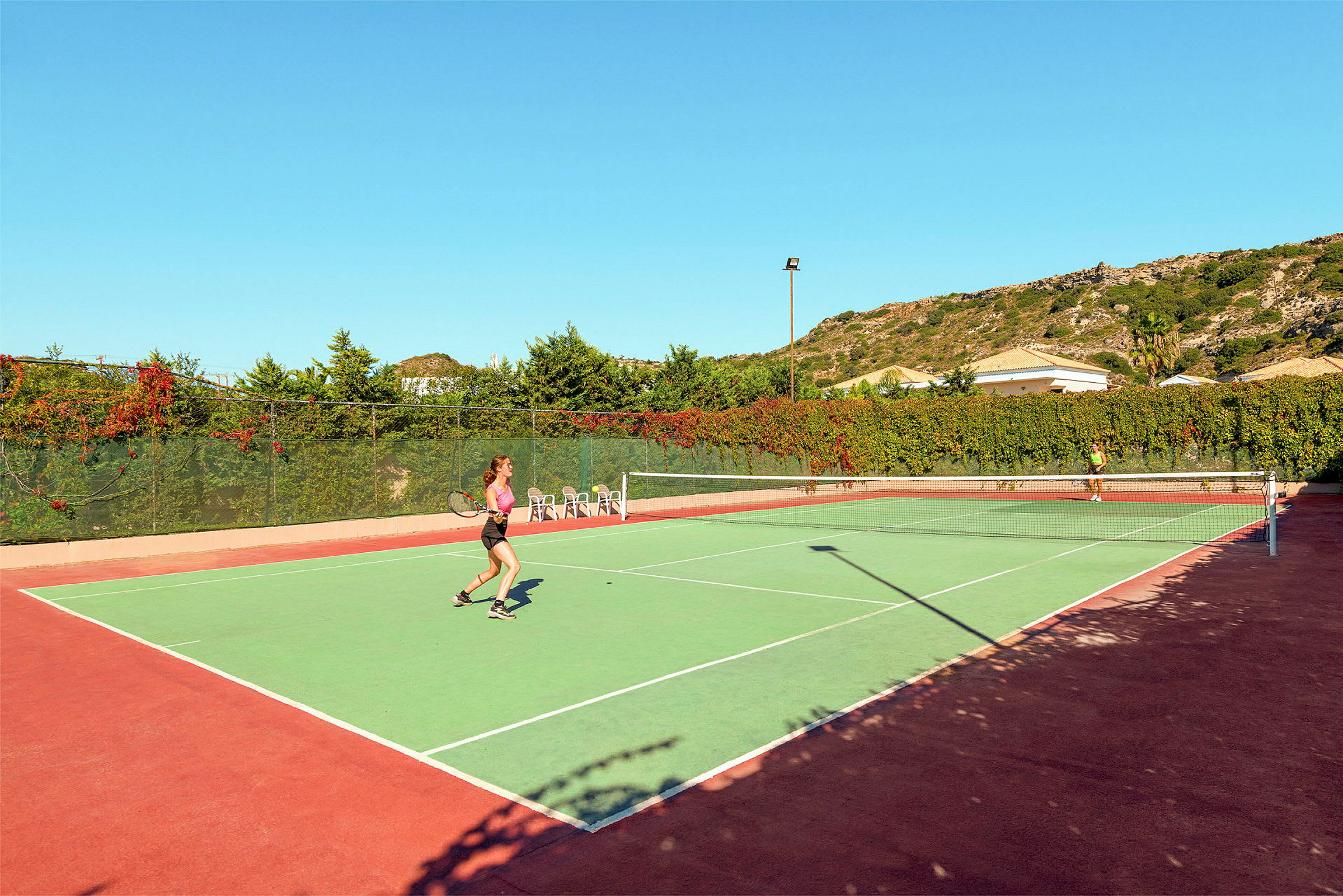 To personer spiller tennis på en utendørsbane under klar himmel. (AI-generert tekst)