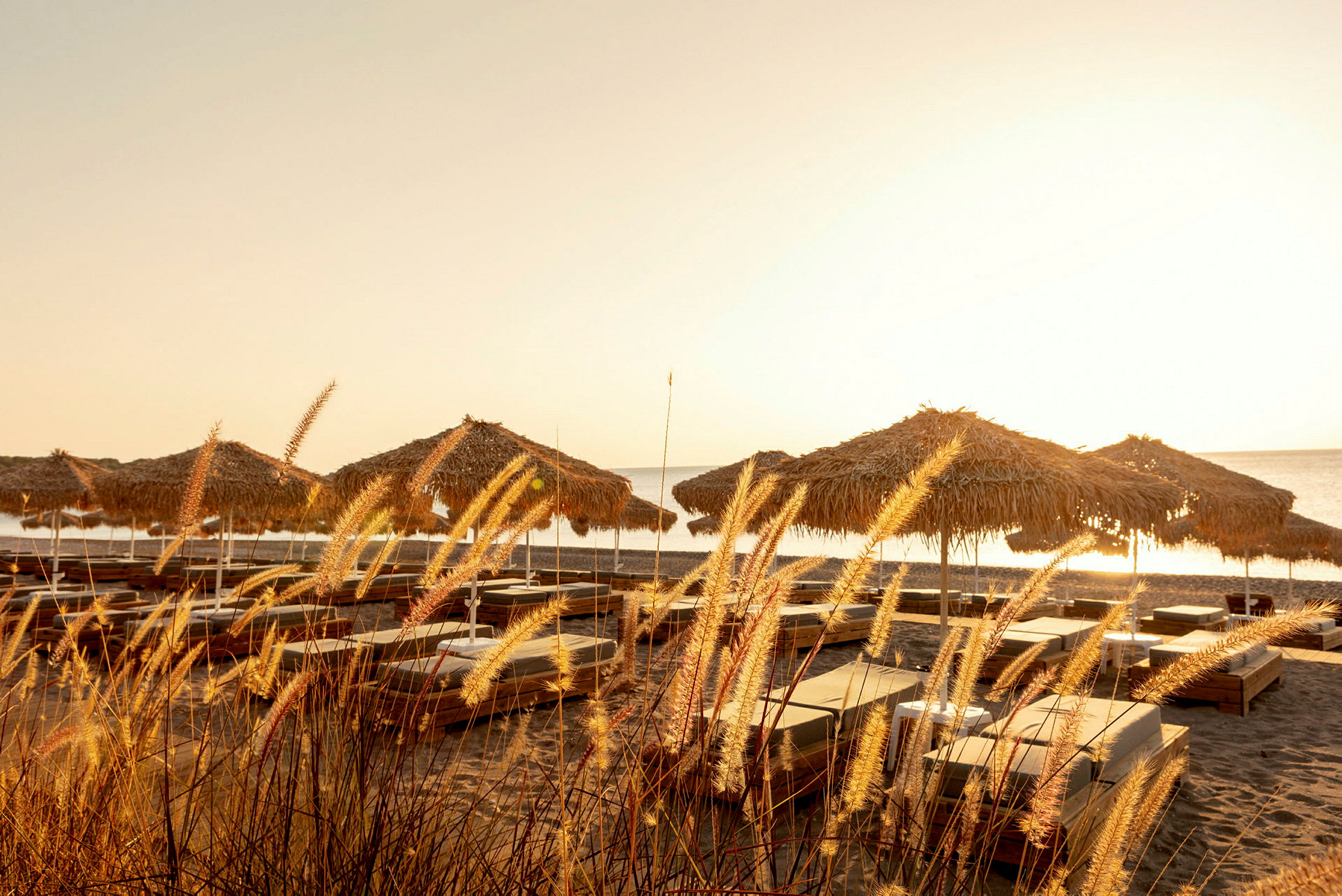 Bilde av solsenger og parasoller på en sandstrand under solnedgang. (AI-generert tekst)
