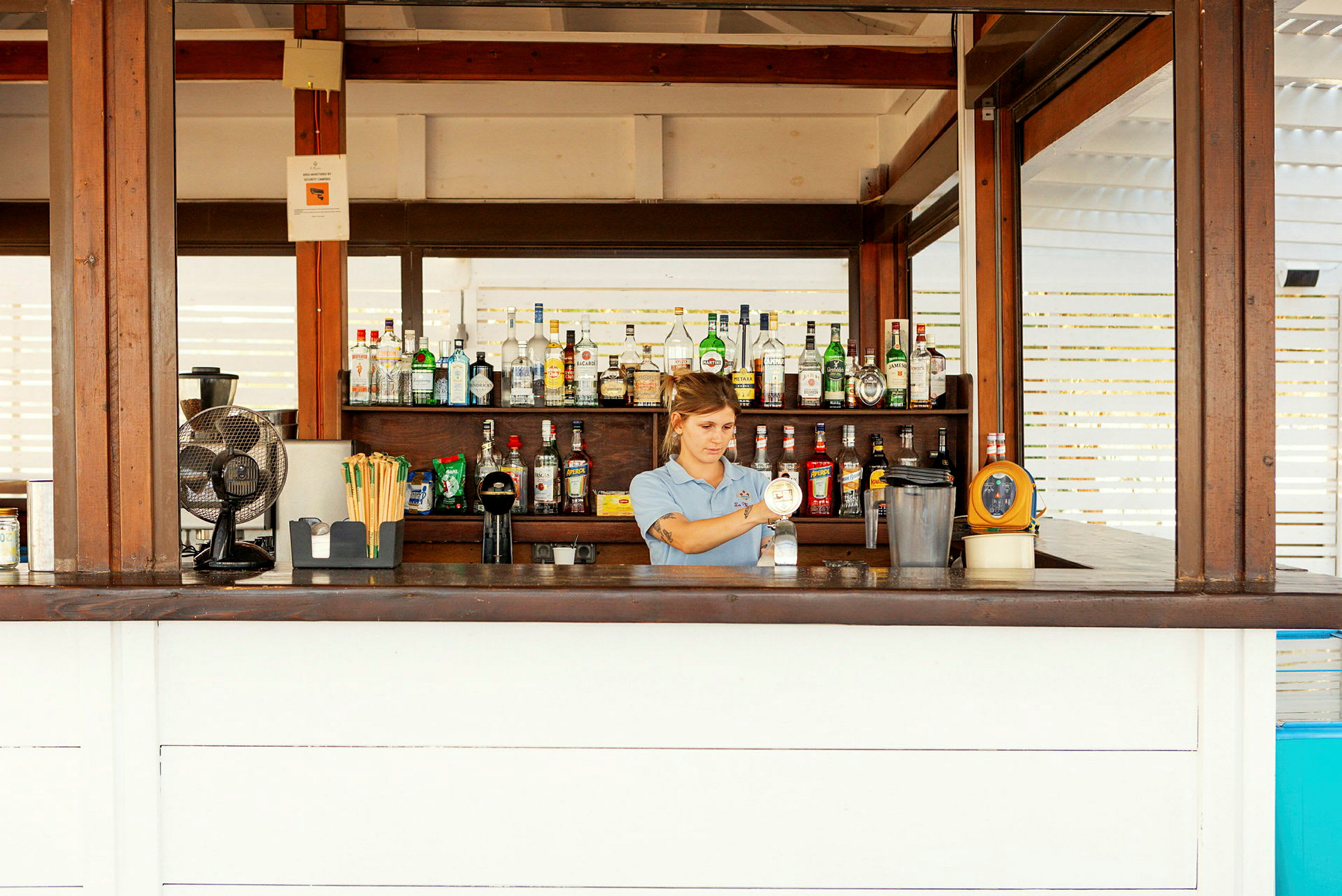 En bar med forskjellige flasker organisert på hyller bak disken. (AI-generert tekst)