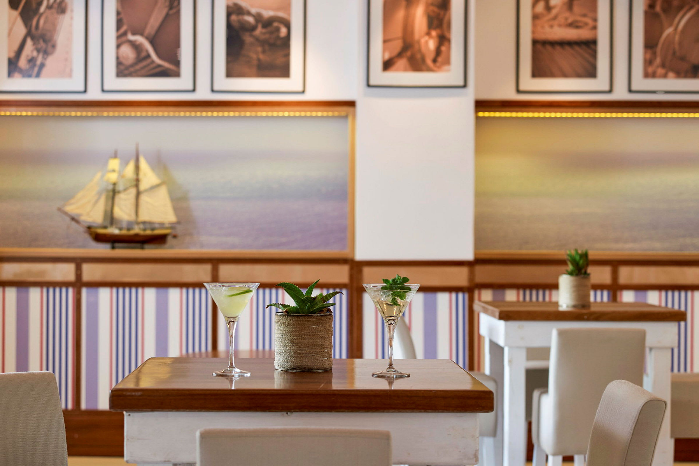 Bord med cocktailglass og planter, interiøret viser en modell av seilbåt og panoramabilder. (AI-generert tekst)