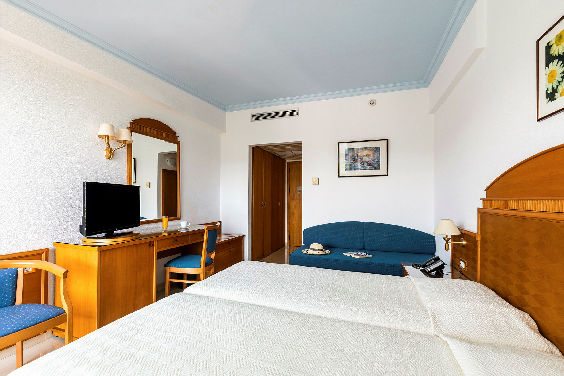 Et hotellrom med en seng, en sofa, et skrivebord og en TV. (AI-generert tekst)