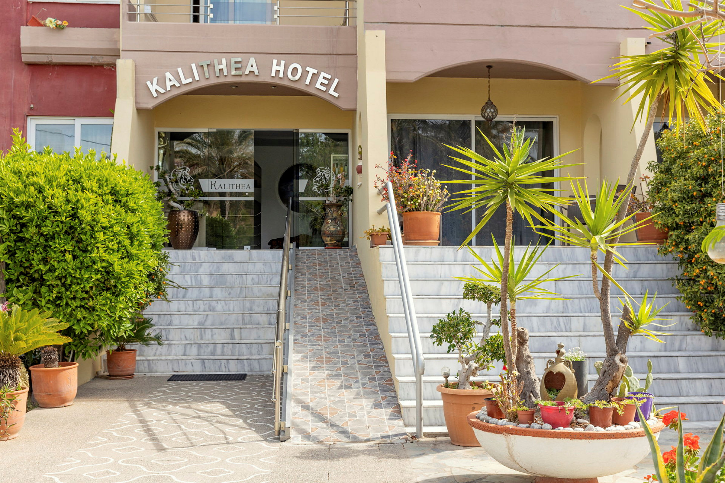 Inngangen til Kalithea Hotel med trapper og beplantning i forgrunnen. (AI-generert tekst)