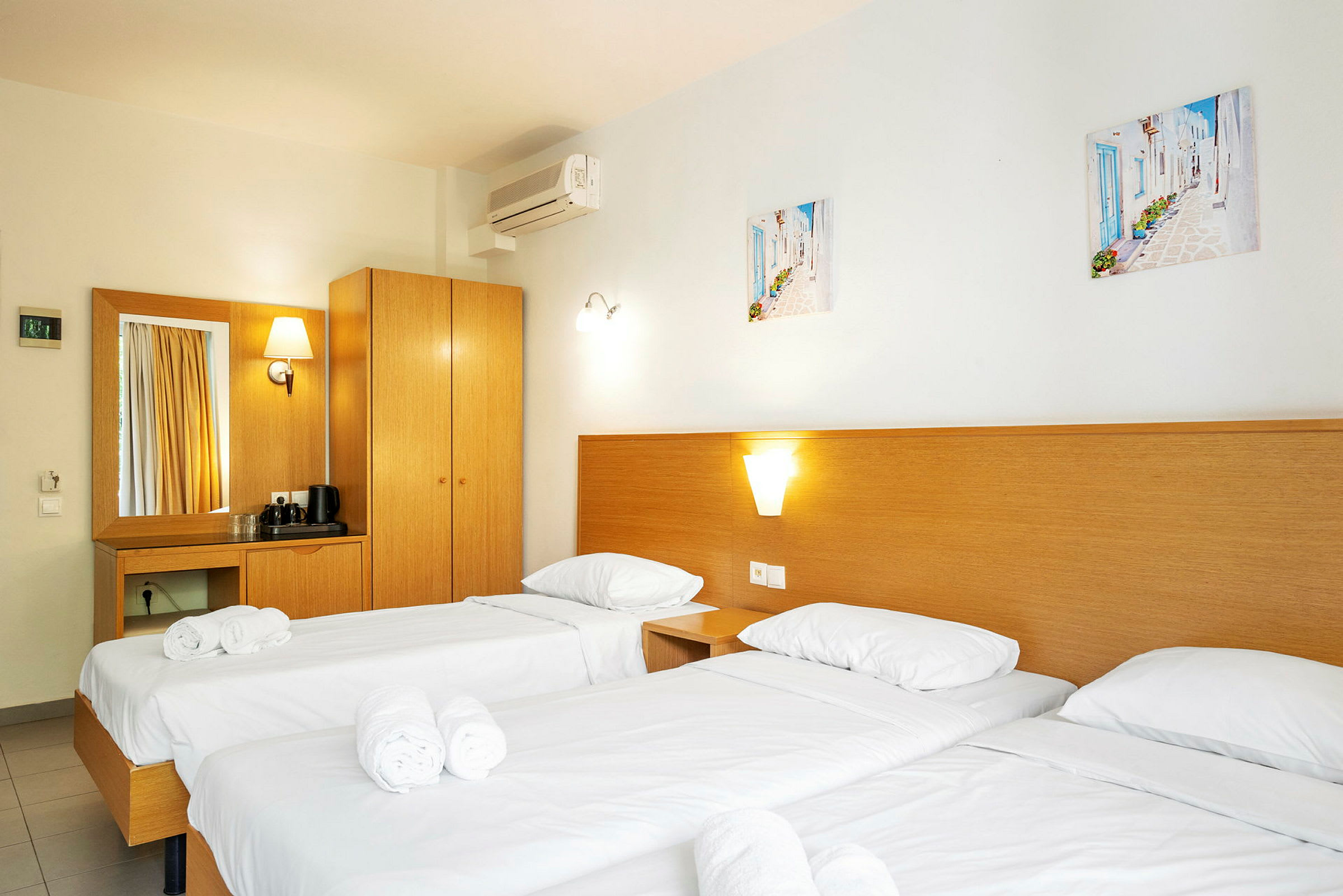Hotellrom med tre enkeltsenger, innredet med hvitt sengetøy og rullede håndklær. (AI-generert tekst)