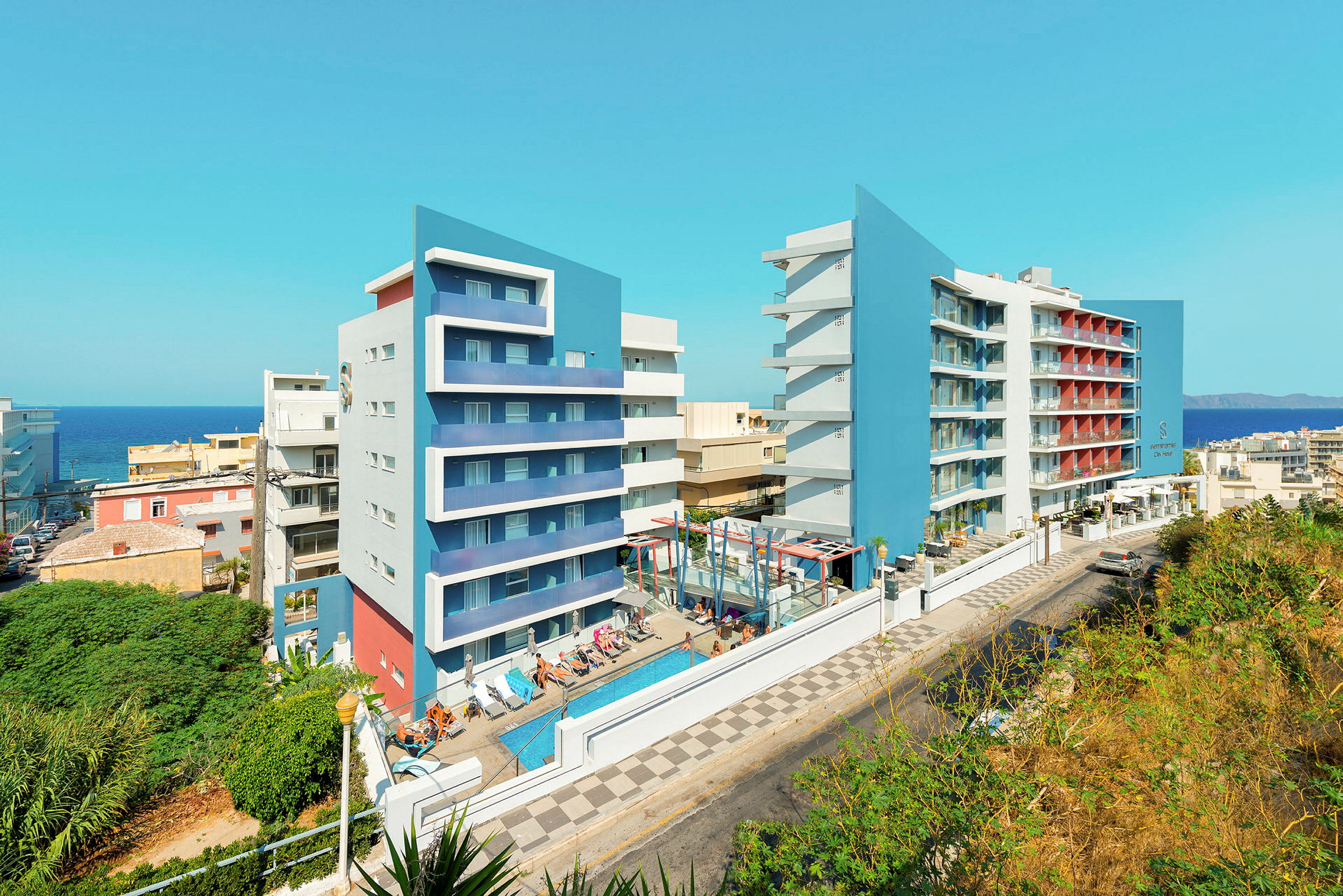 Bilde av to moderne hotellbygninger med blå fasader, et basseng og solsenger i forgrunnen. (AI-generert tekst)