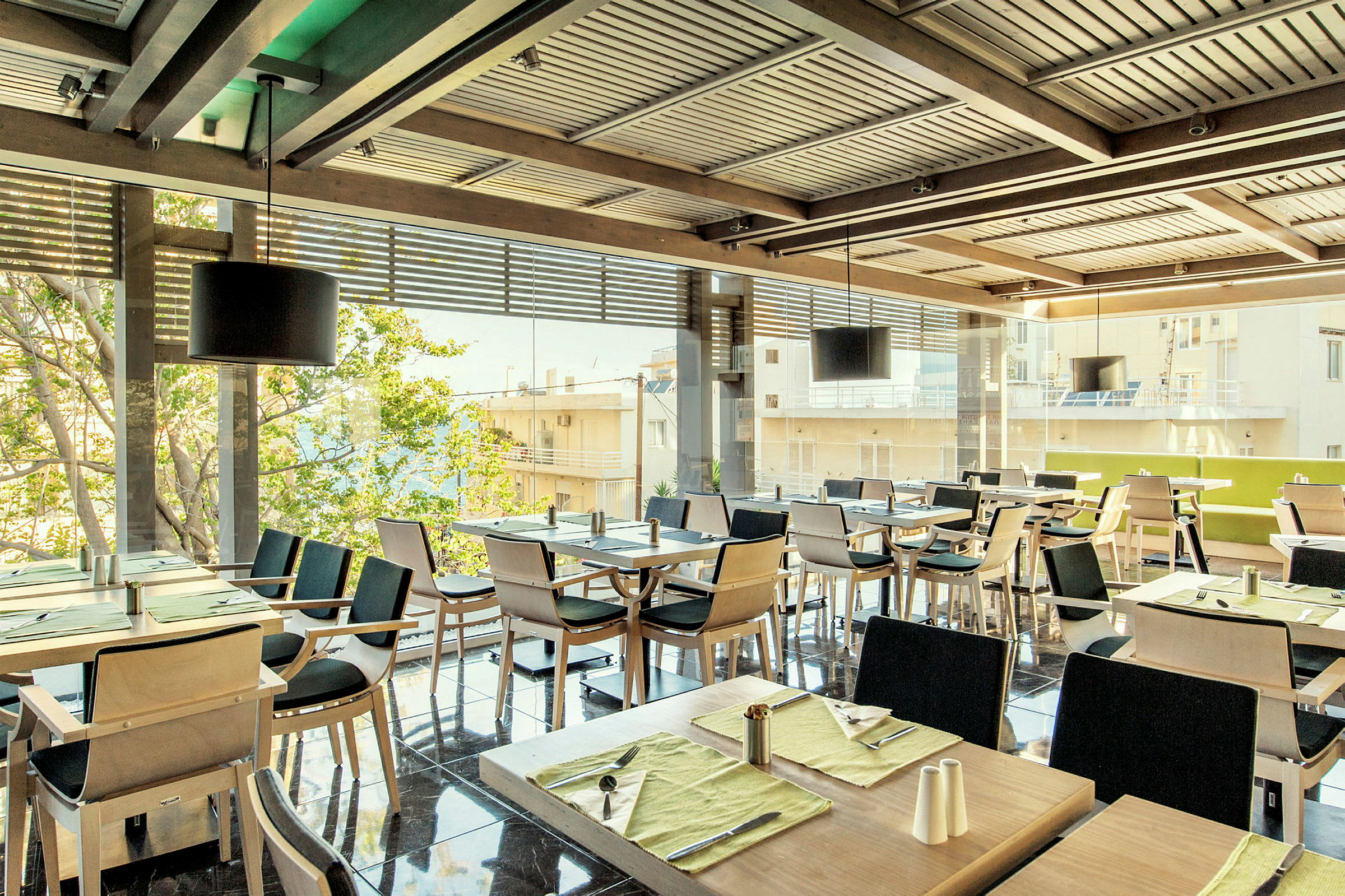 En restaurant med flere dekkede bord og stoler, med vinduer mot en byutsikt. (AI-generert tekst)