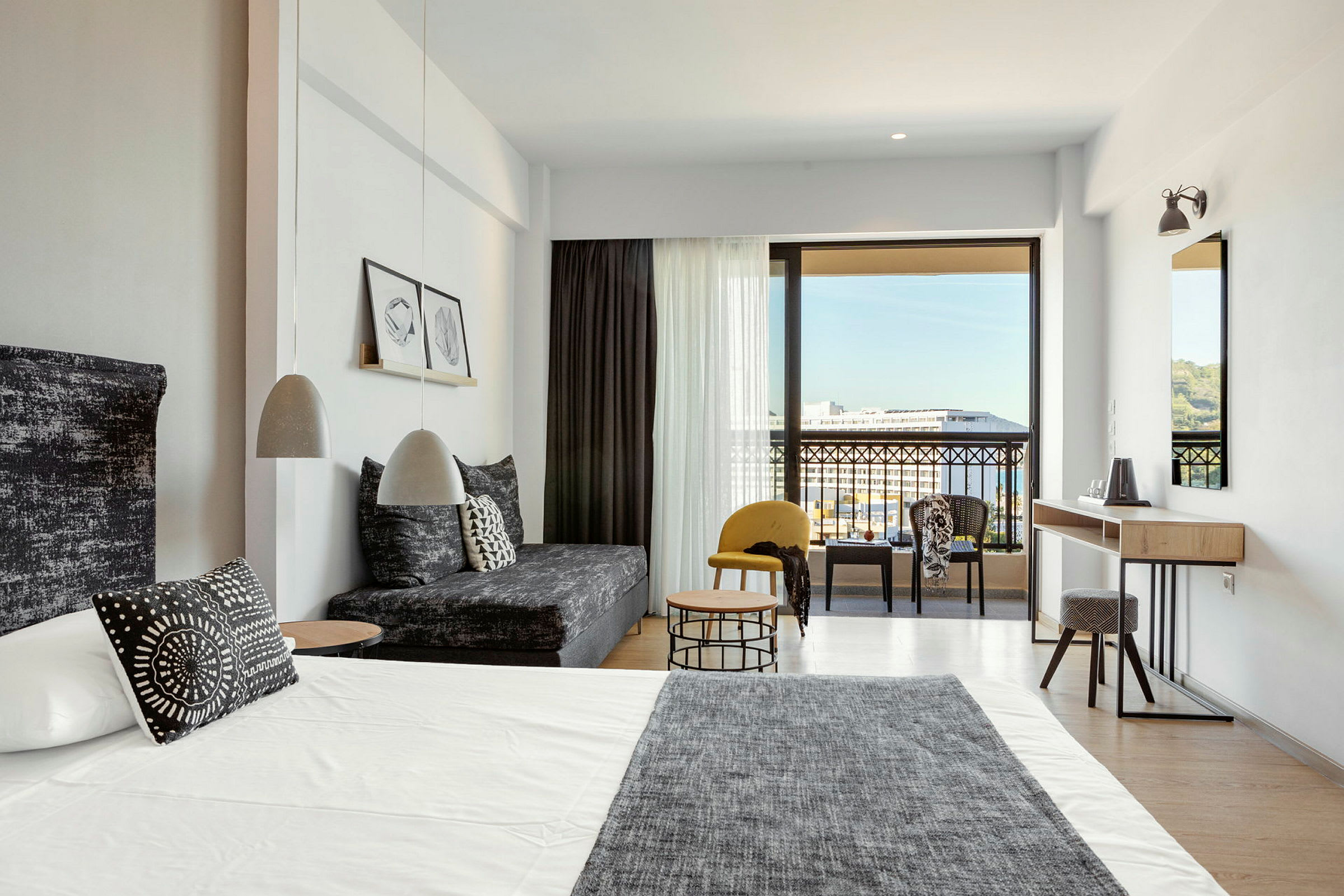 Moderne hotellrom med seng, sofa og sittegruppe samt utsikt mot balkong og omgivelser. (AI-generert tekst)