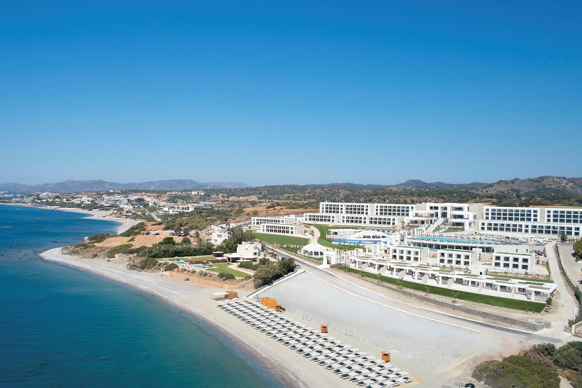 Luftfoto av en kystlinje med hotellkompleks og stranden i forgrunnen. (AI-generert tekst)
