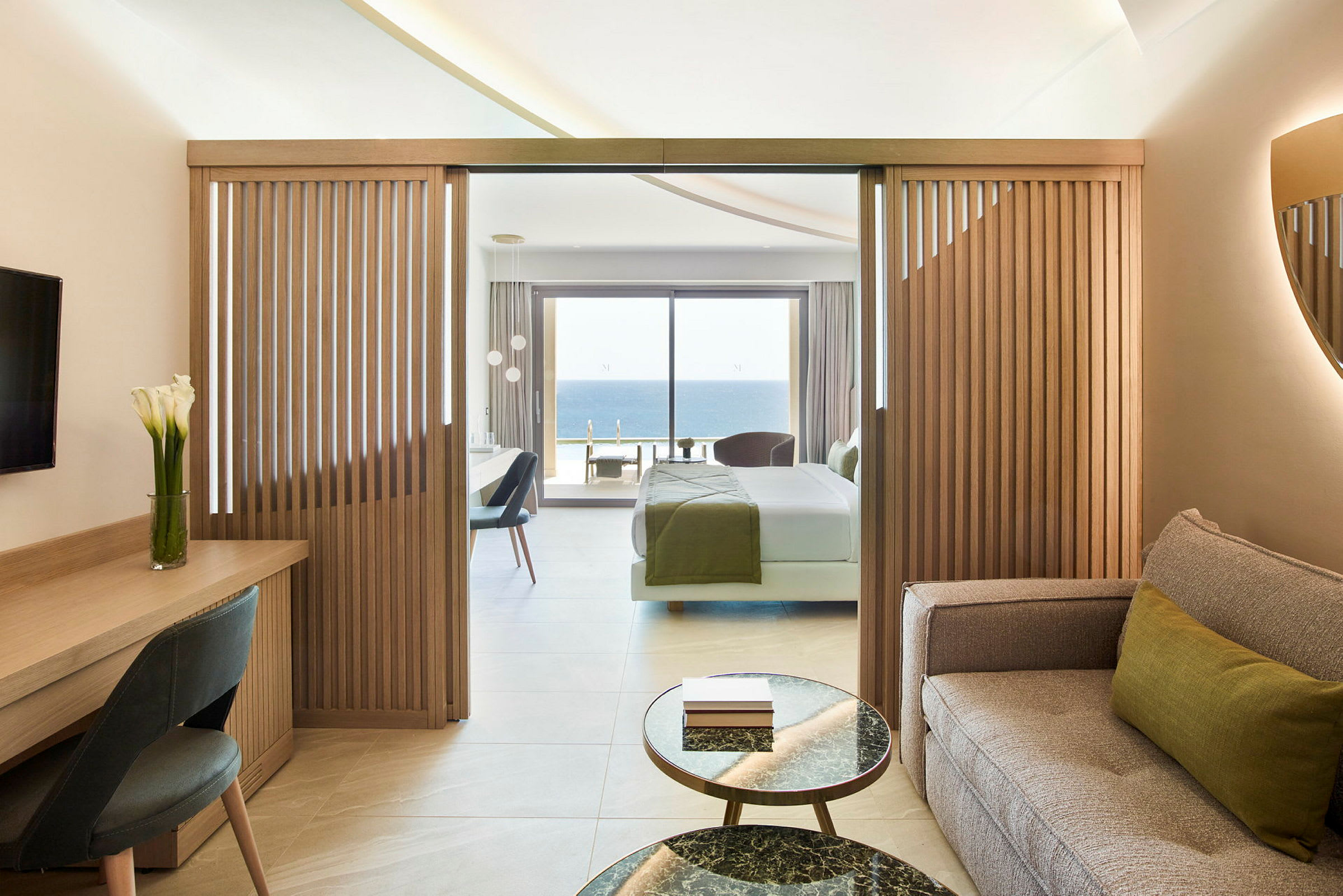 Et hotellrom med sittegruppe, arbeidsbord og soverom med utsikt mot havet. (AI-generert tekst)