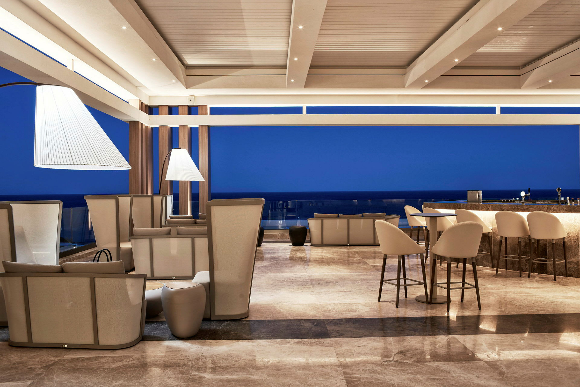 En moderne lounge med sitteplasser og bardisk, med blå himmel i bakgrunnen. (AI-generert tekst)