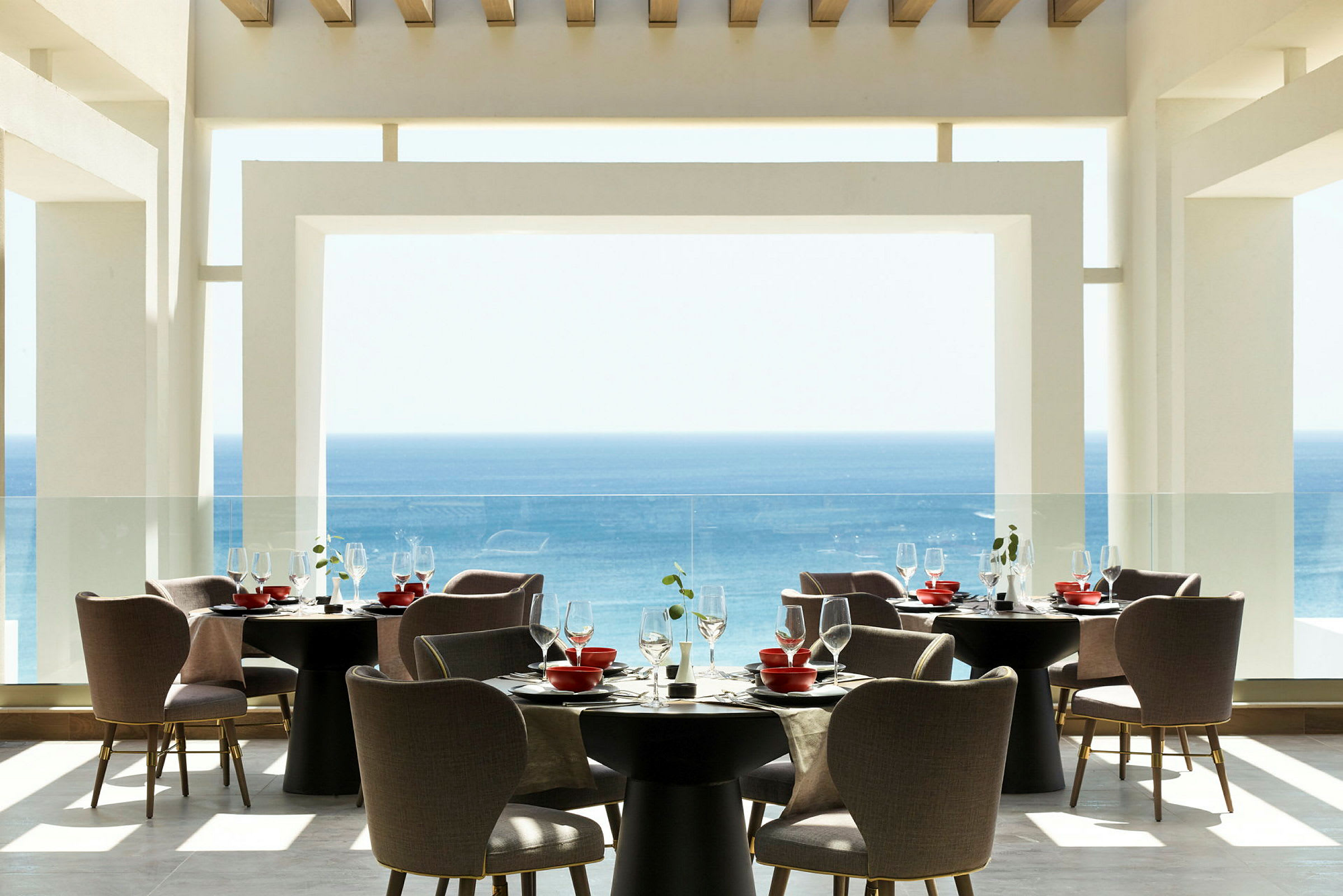 En moderne restaurant med utsikt over havet, møblert med runde bord og komfortable stoler. (AI-generert tekst)