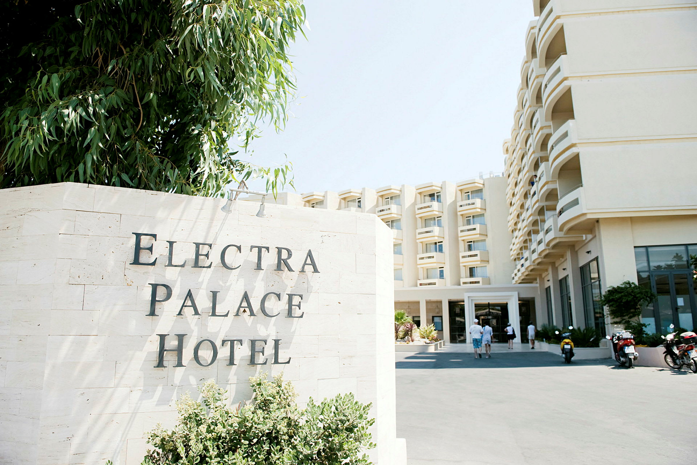 Hotellfasade med skiltet 'Electra Palace Hotel' foran. (AI-generert tekst)