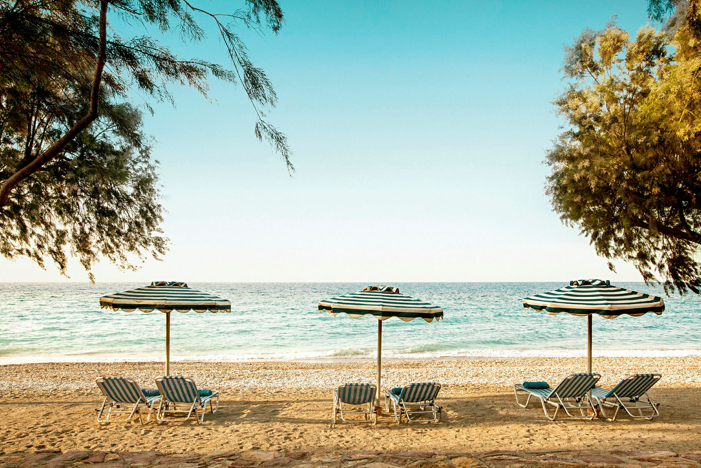 Strand med parasoller og solsenger ved havet. (AI-generert tekst)