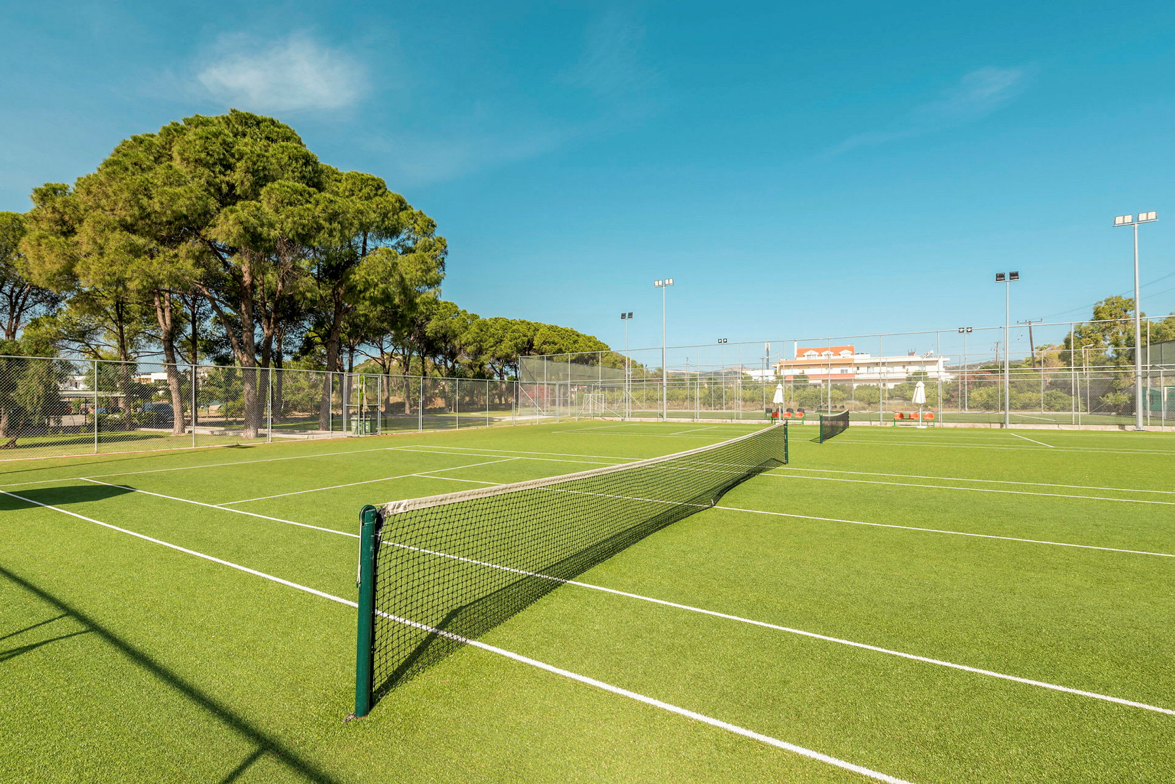 En grønn tennisbane med nett og omkringliggende gjerde. (AI-generert tekst)