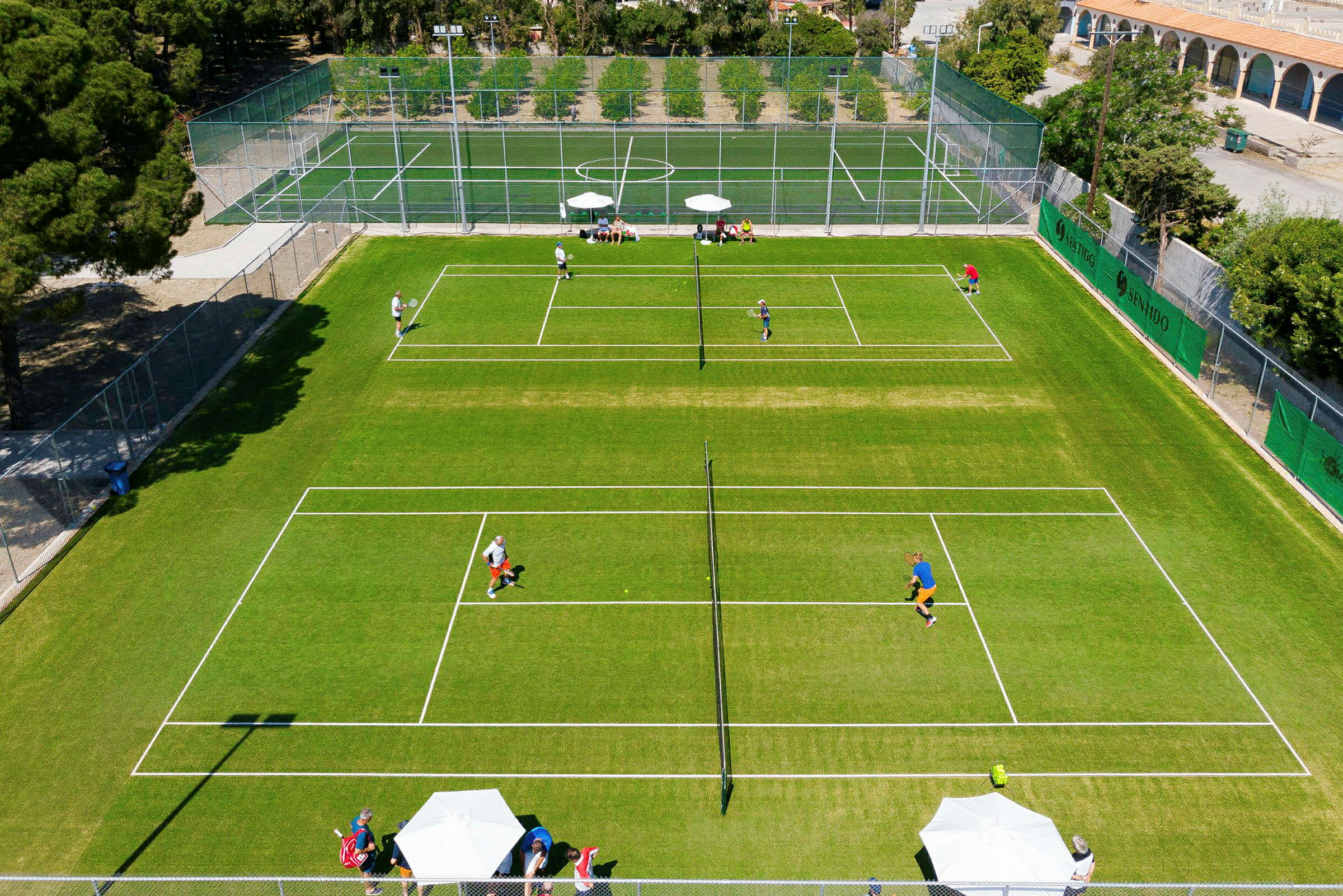 Luftfoto av en tennisbane med spillere og omgivende trær. (AI-generert tekst)
