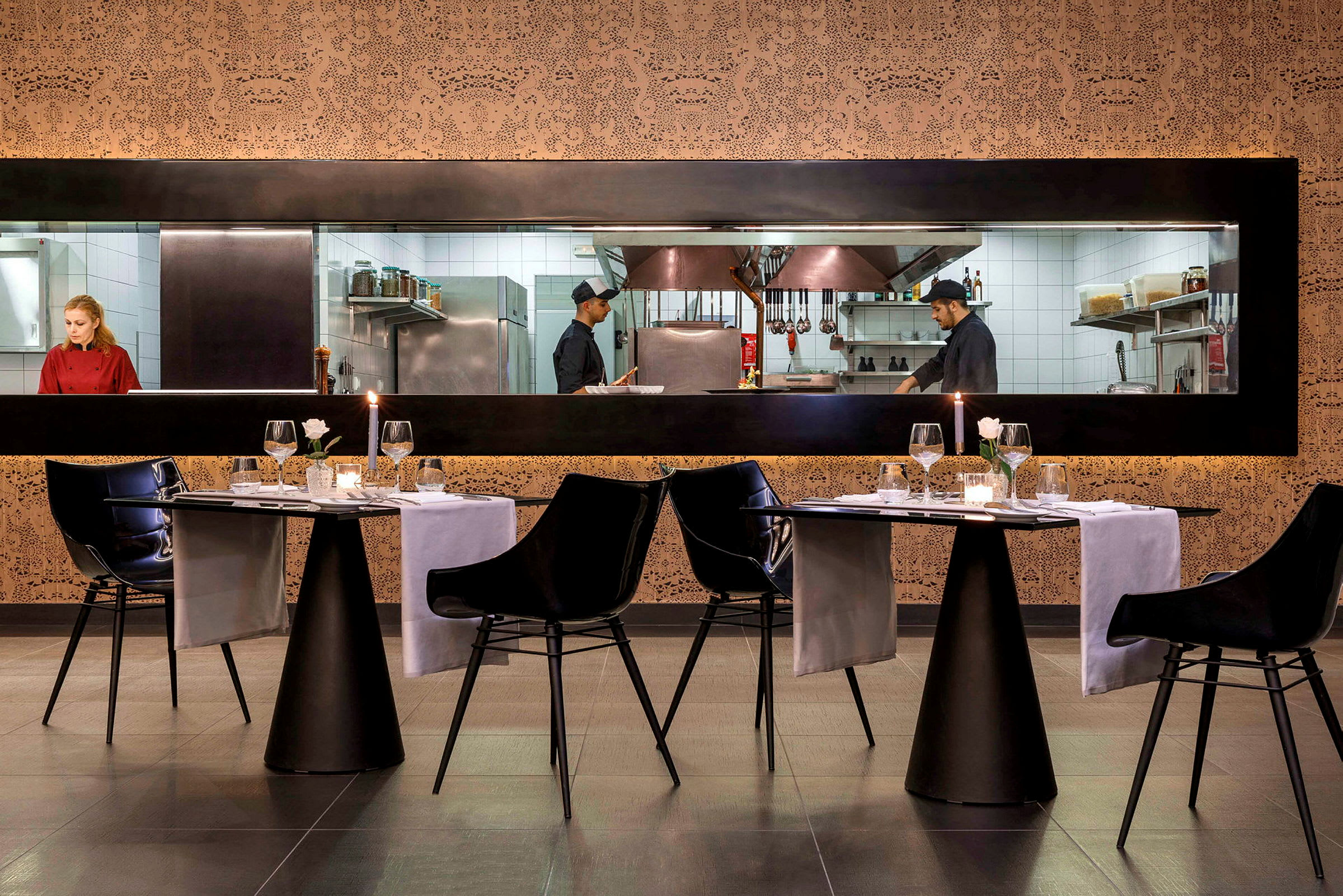 Bilde av en restaurant med opplyste bordoppsett og synlig kjøkken gjennom et glassvindu. (AI-generert tekst)