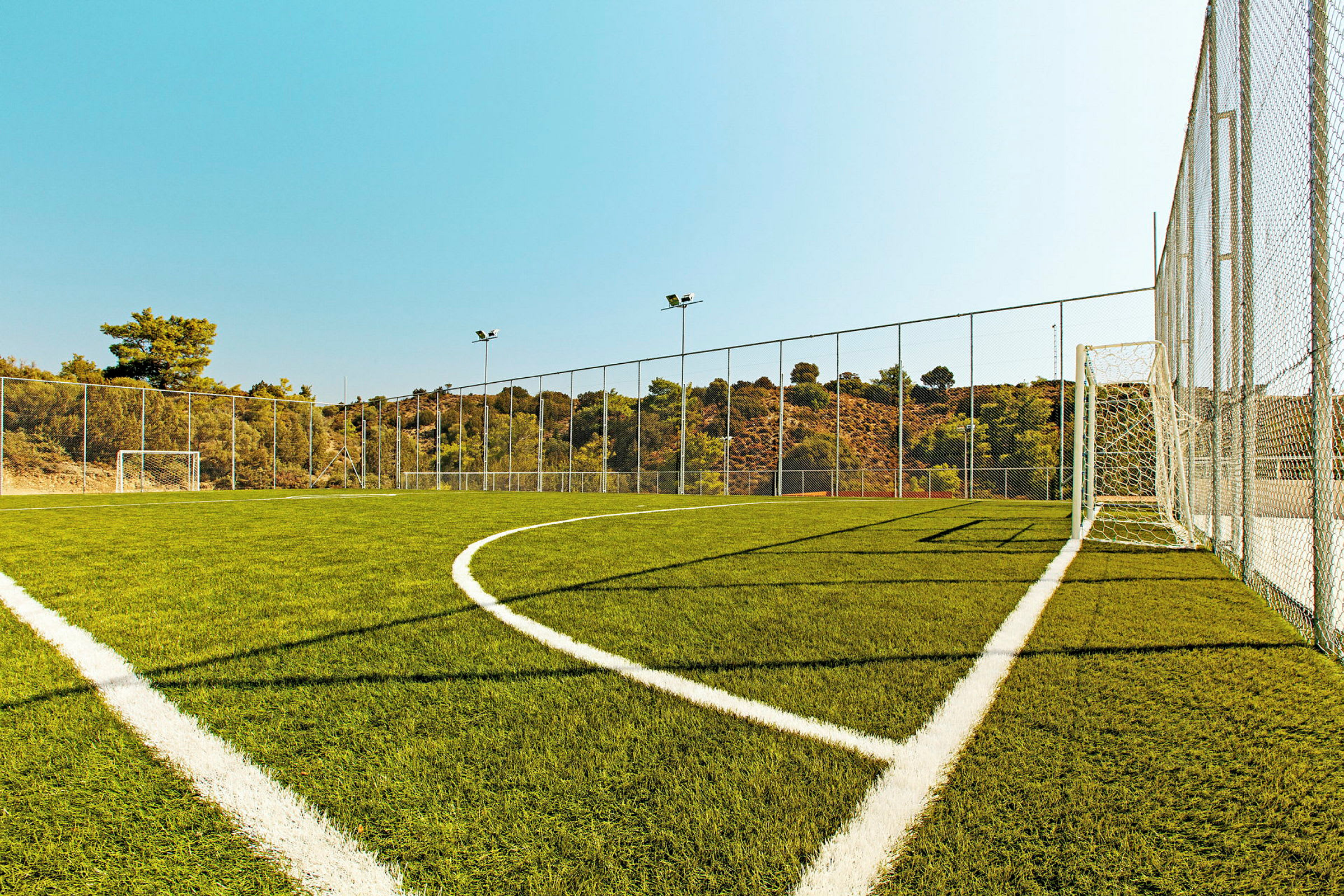 Fotballbane med grønt gress, hvite linjer og målburer omgitt av nett. (AI-generert tekst)