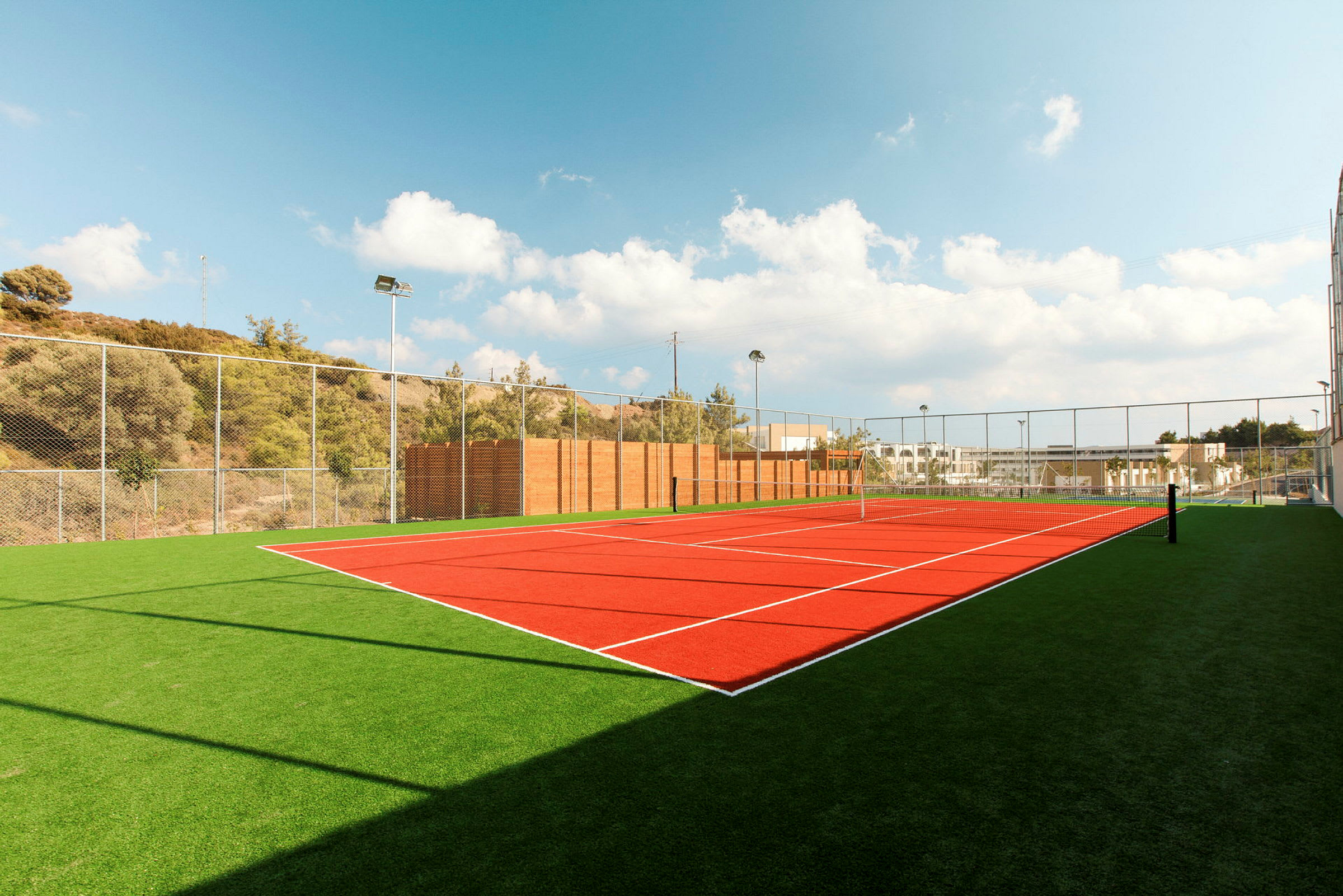 Bilde av en utendørs tennisbane med kunstgress og nett under en klar blå himmel. (AI-generert tekst)
