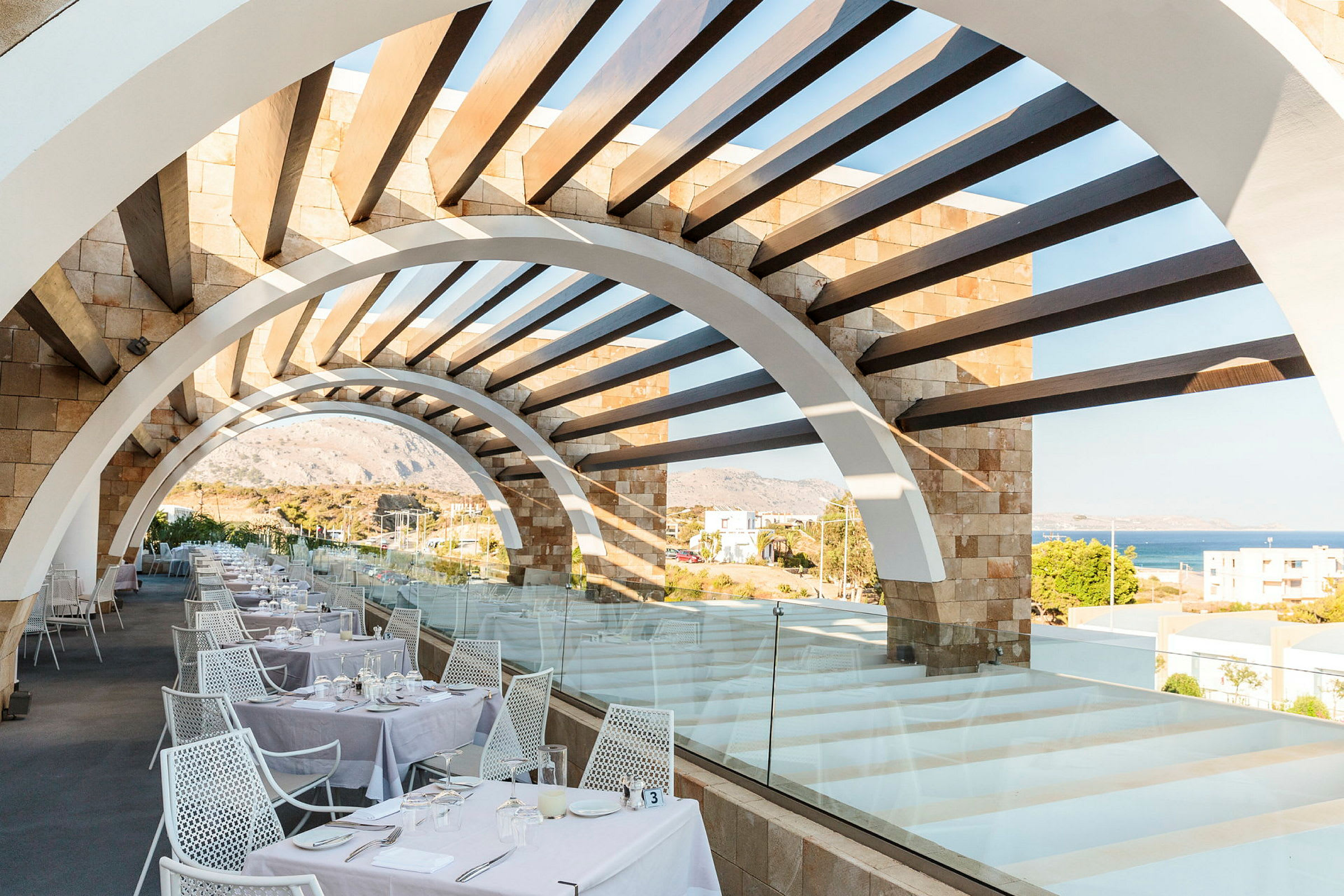 Restaurantterrasse med buet pergola og havutsikt. (AI-generert tekst)