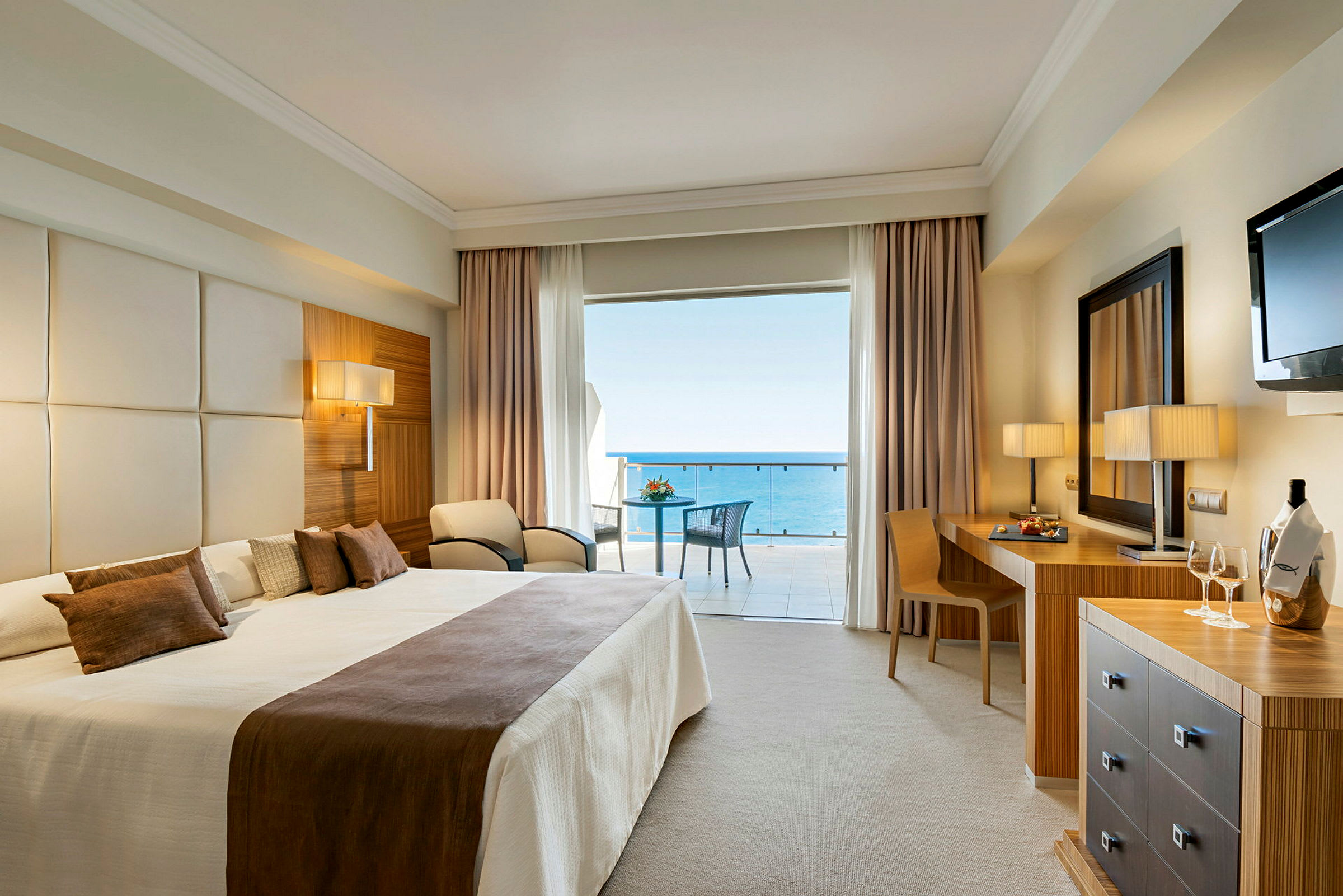 Hotellrom med stor dobbeltseng og utsikt mot havet fra balkongen. (AI-generert tekst)