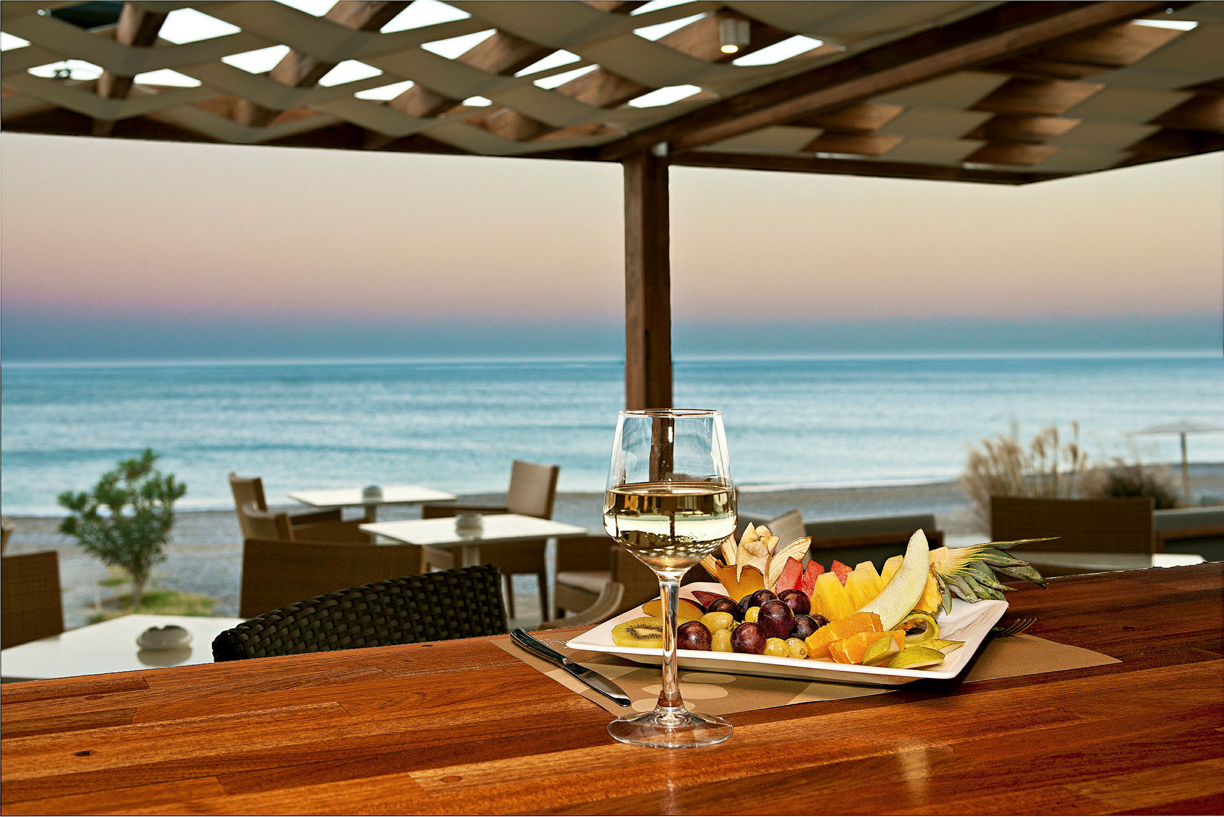 En tallerken med frisk frukt og et glass hvitvin står på et bord med utsikt over havet. (AI-generert tekst)