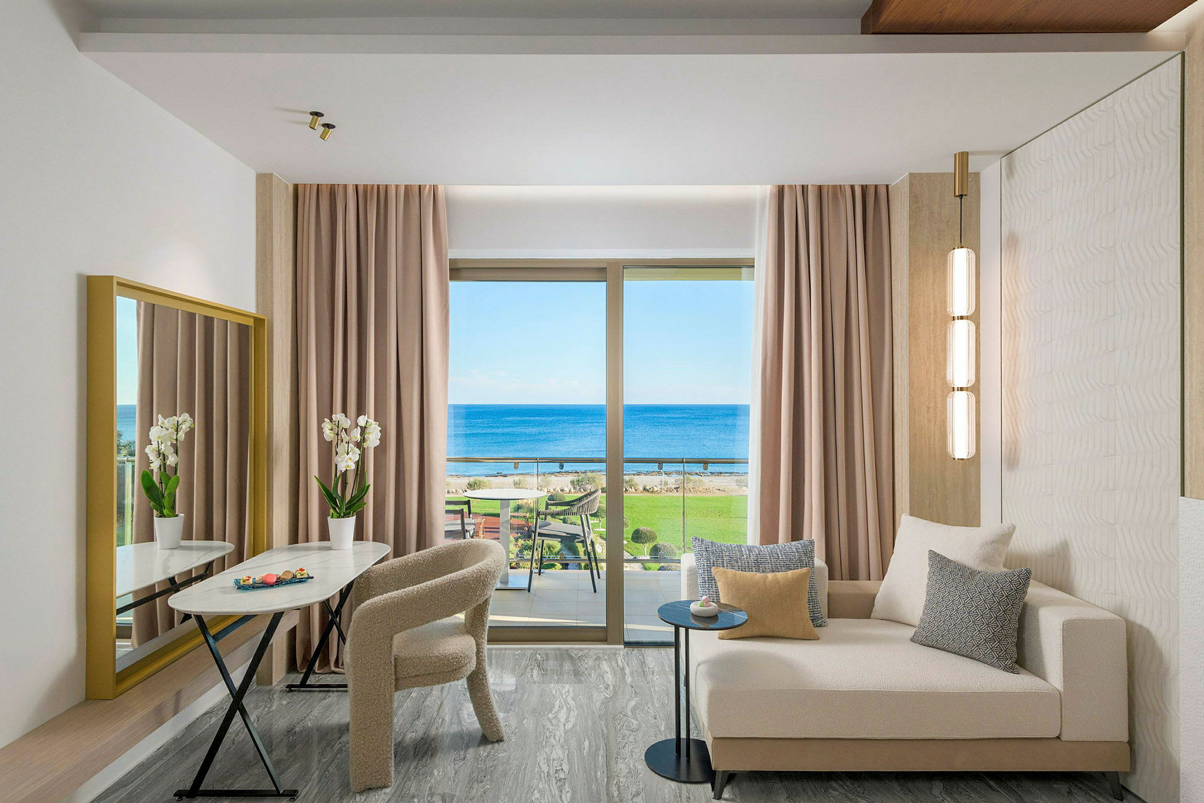En moderne hotellsuite med sofa, bord, stoler og utsikt over havet gjennom et stort vindu. (AI-generert tekst)