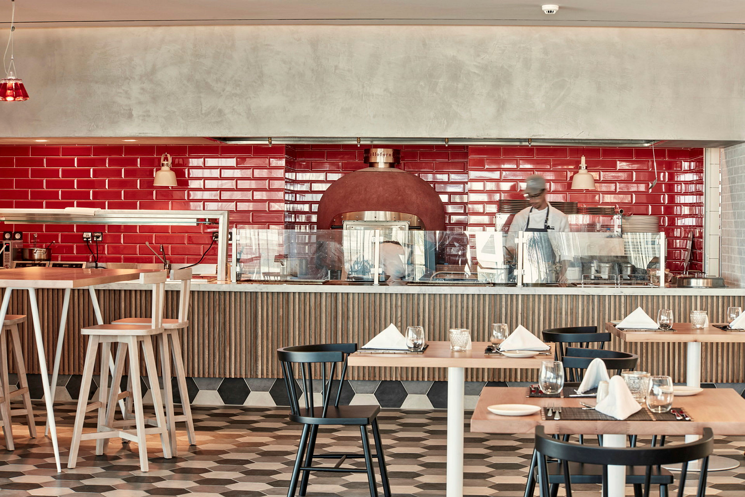 En restaurantinteriør med rød flislagt vegg, spisebord og stoler samt en vedovn. (AI-generert tekst)