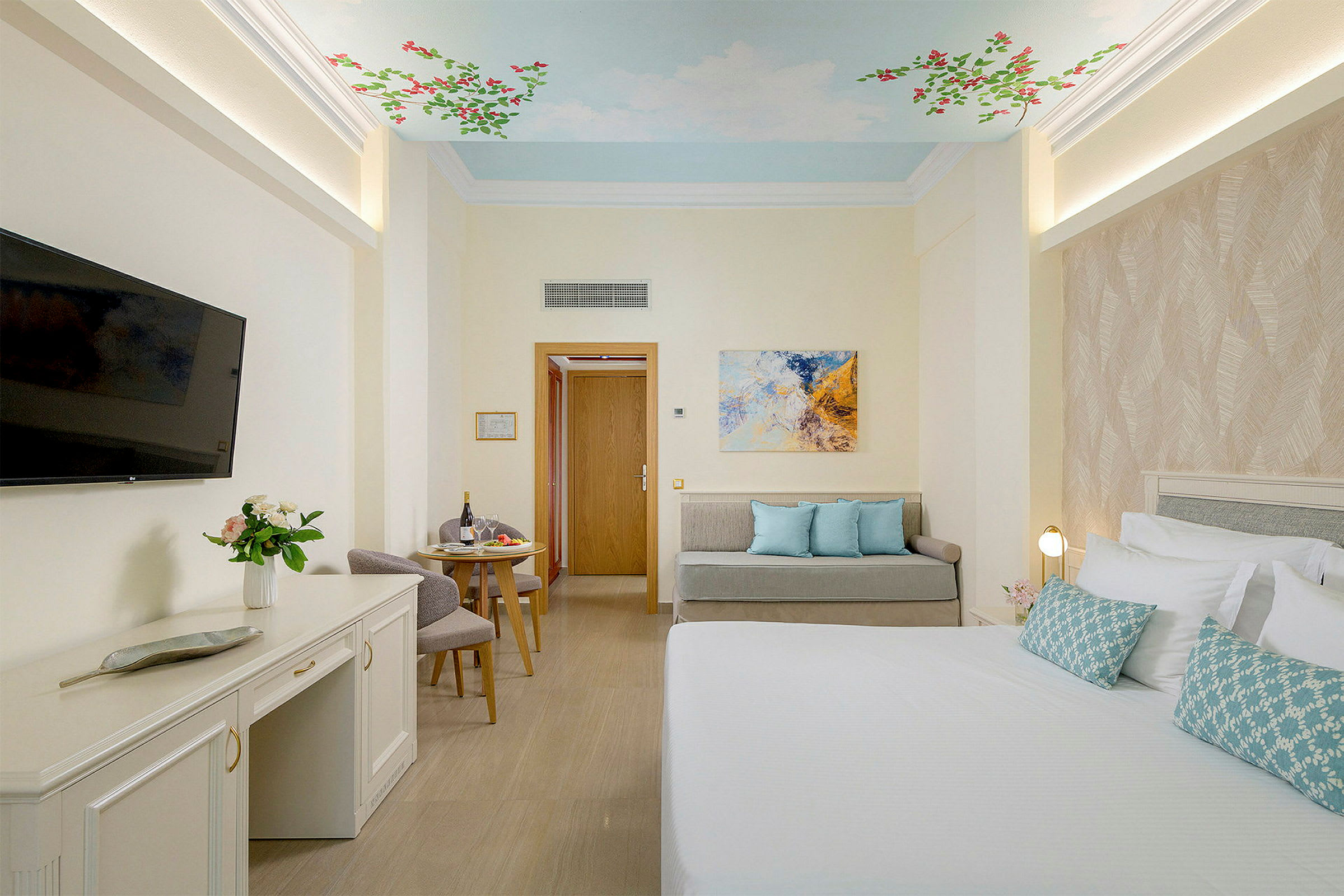 Et hotellrom med en seng, en sittegruppe og et maleri på veggen. Taket har et motiv av himmel og blomster. (AI-generert tekst)