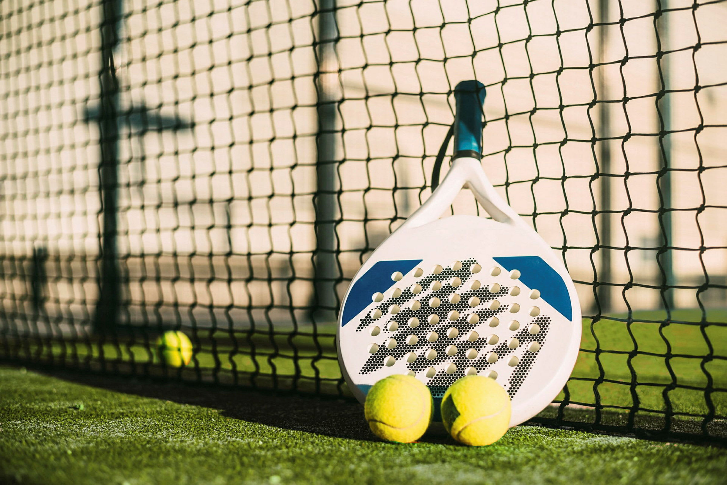En padelracket og to baller ved nettet på en padelbane. (AI-generert tekst)