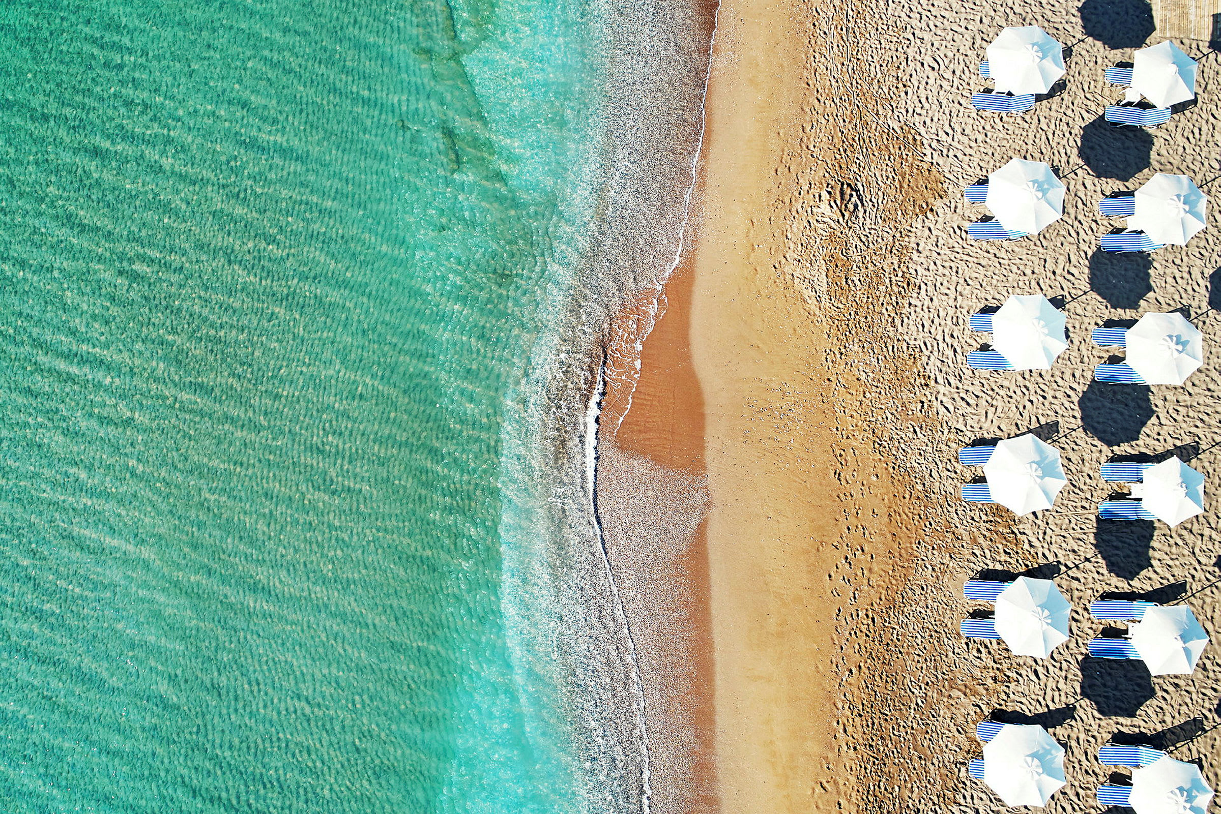 Flyfoto av en strand med parasoller og solsenger ved klart vann. (AI-generert tekst)