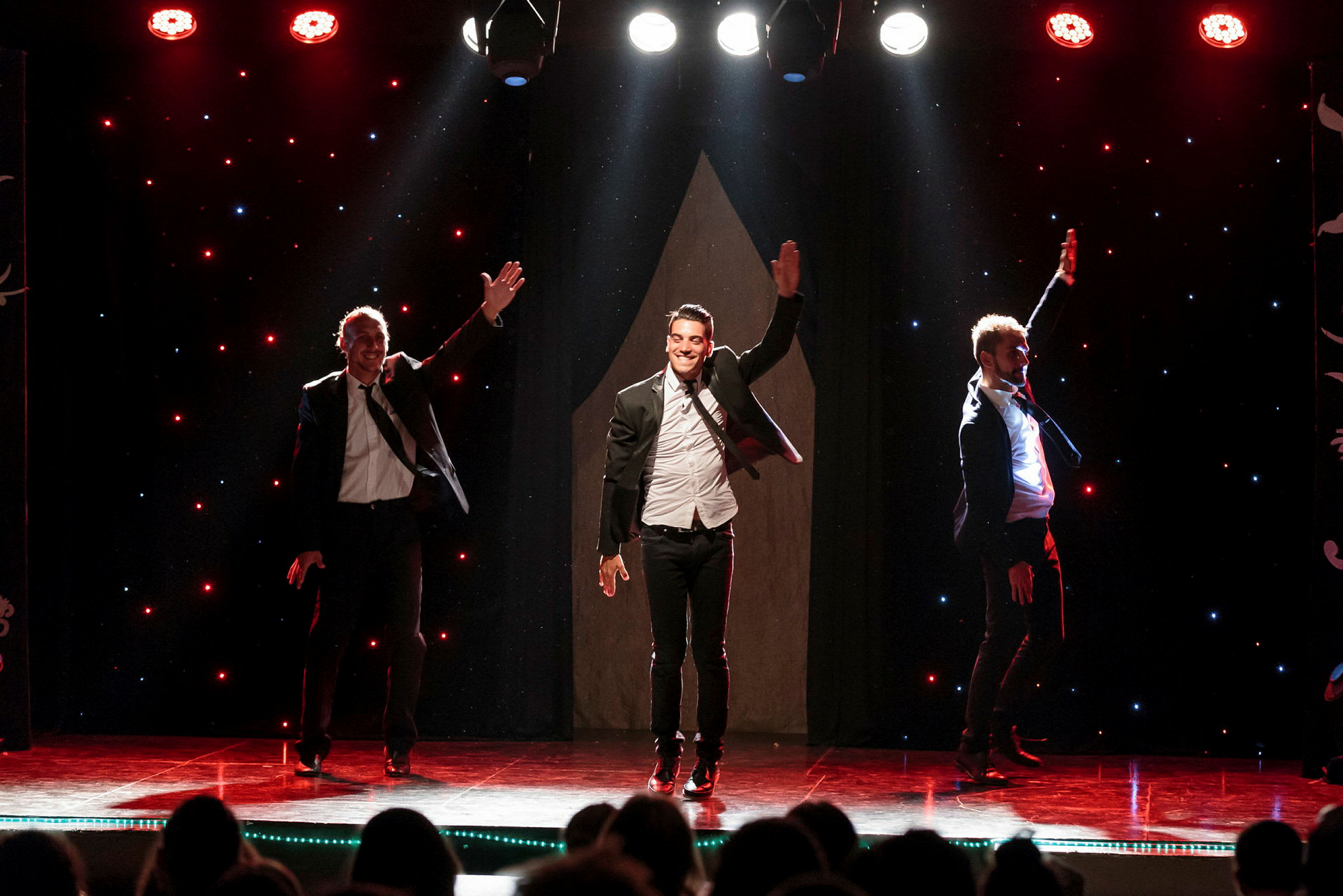 Tre personer utfører en dansforestilling på en scene med lyseffekter. (AI-generert tekst)
