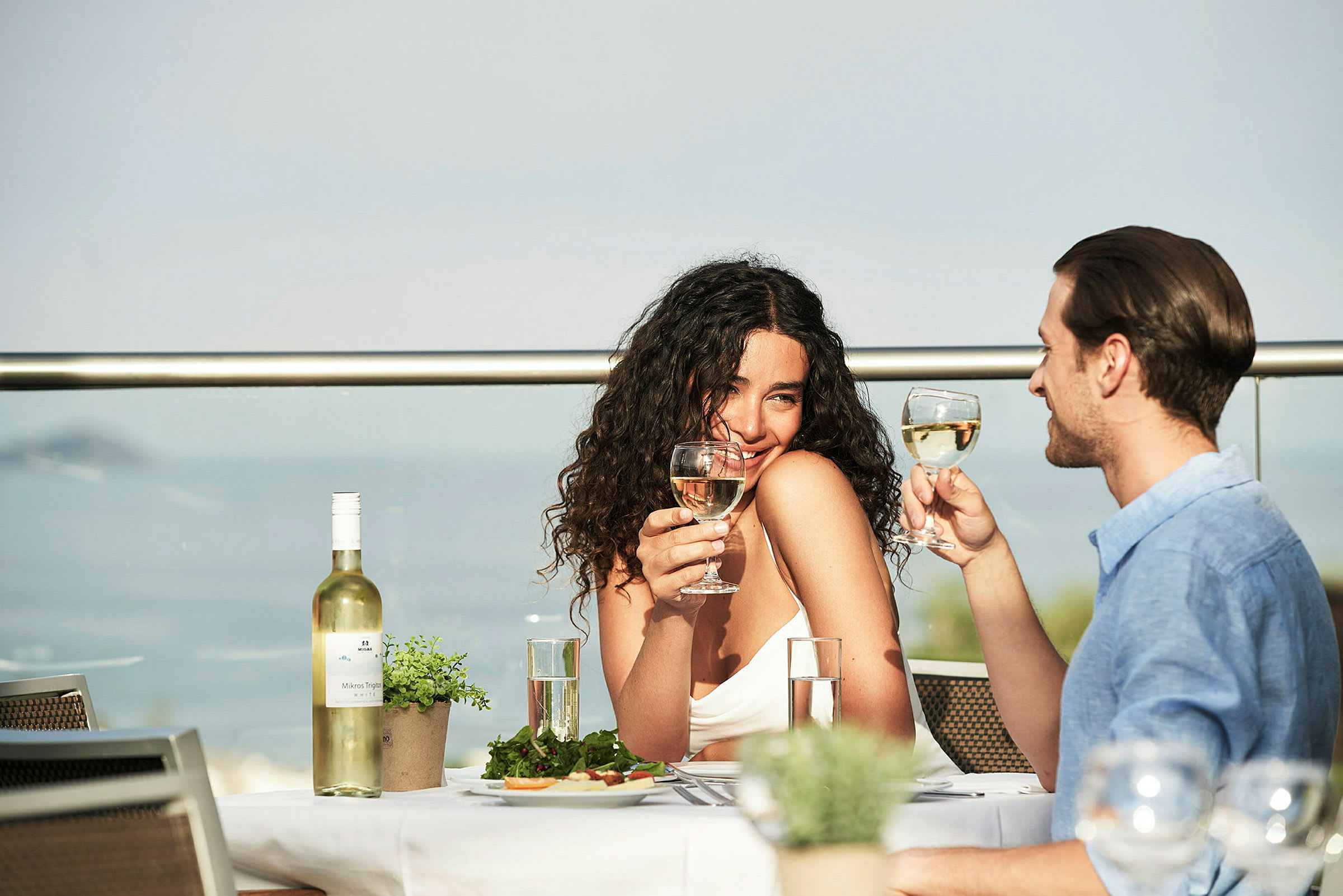 Personer skåler med vinglass ved et dekket bord på en terrasse. (AI-generert tekst)