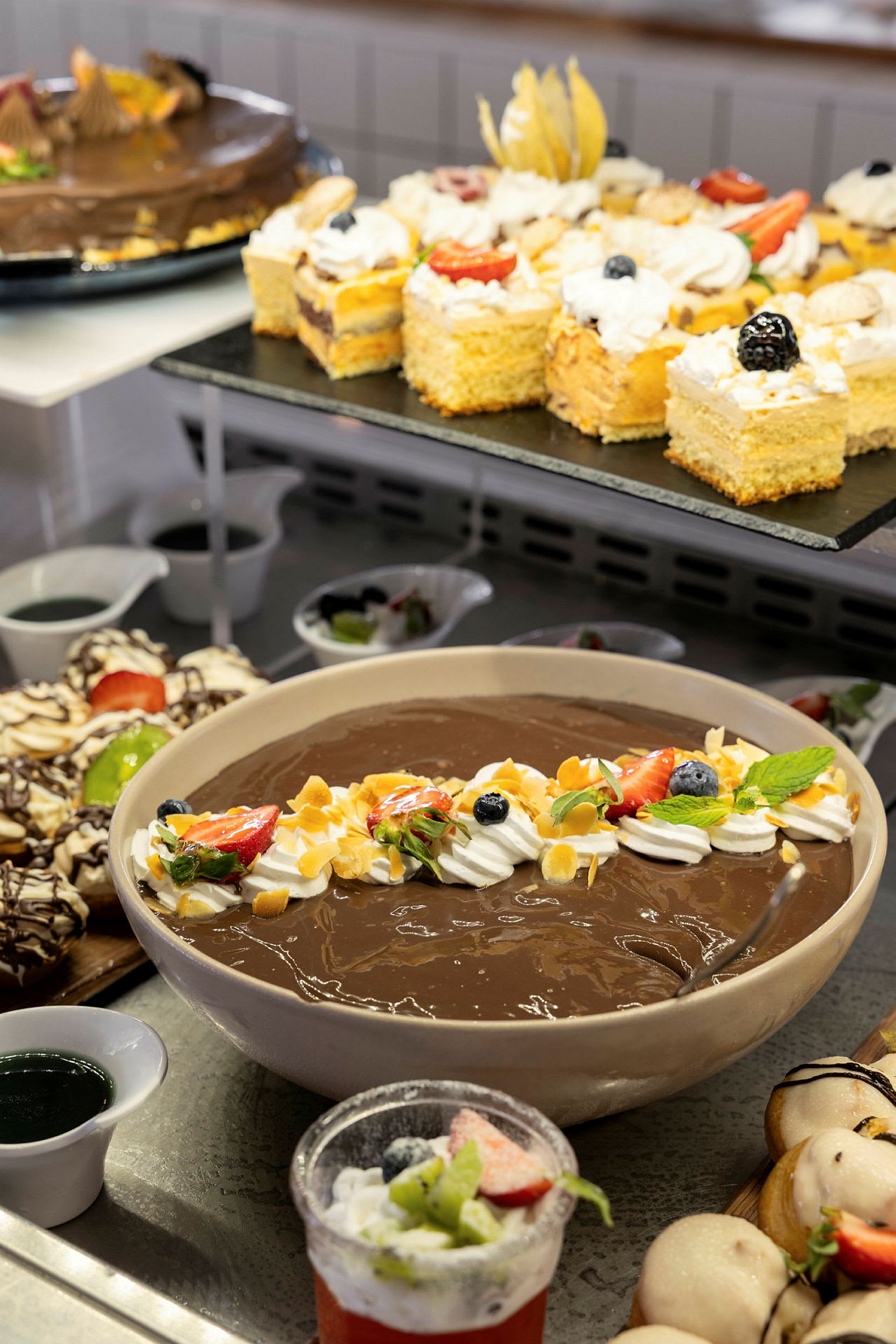 En buffet med forskjellige desserter, inkludert sjokoladepudding pyntet med frukt og krem. (AI-generert tekst)