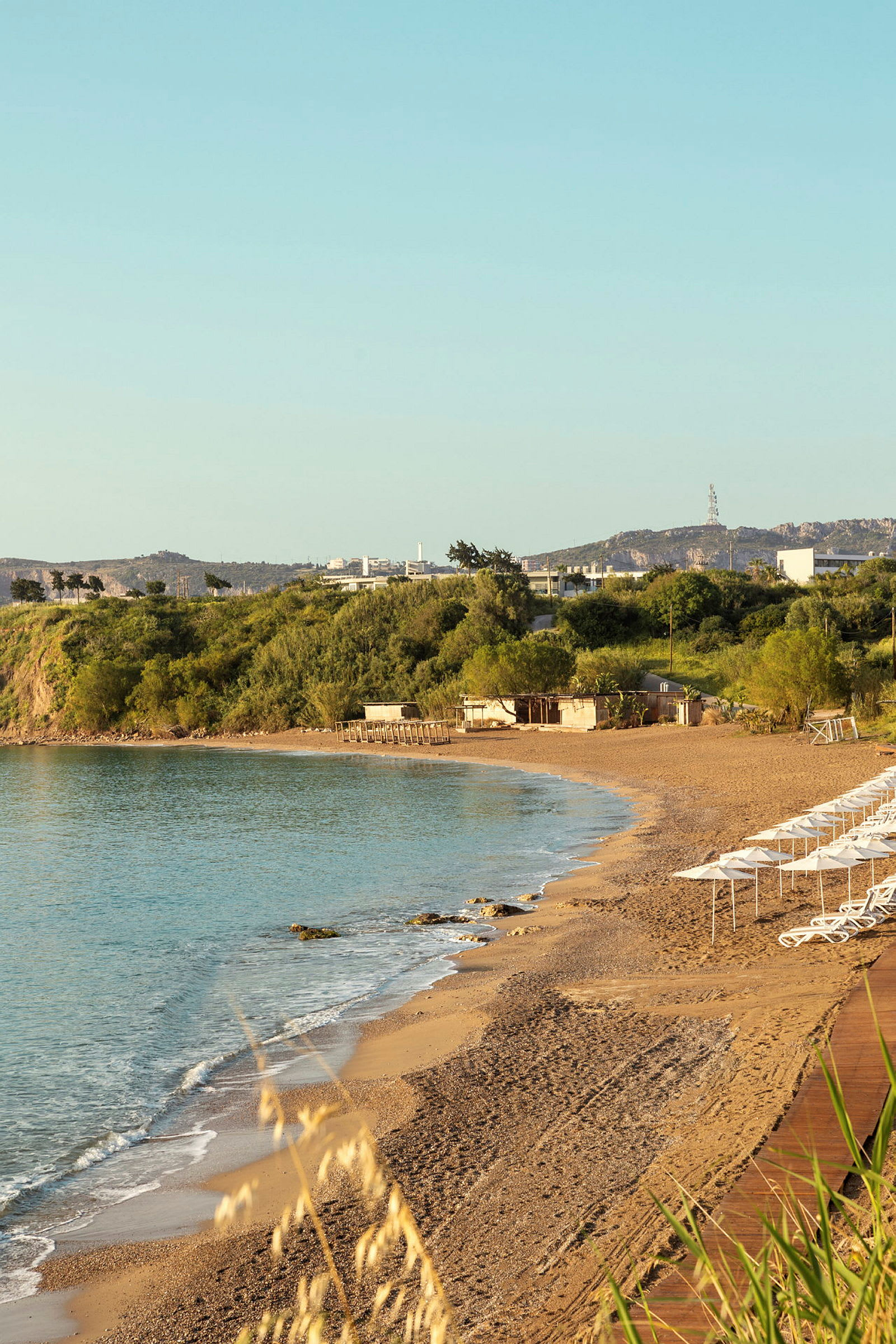 Strand med parasoller og solsenger ved havet, omgitt av grøntområder. (AI-generert tekst)