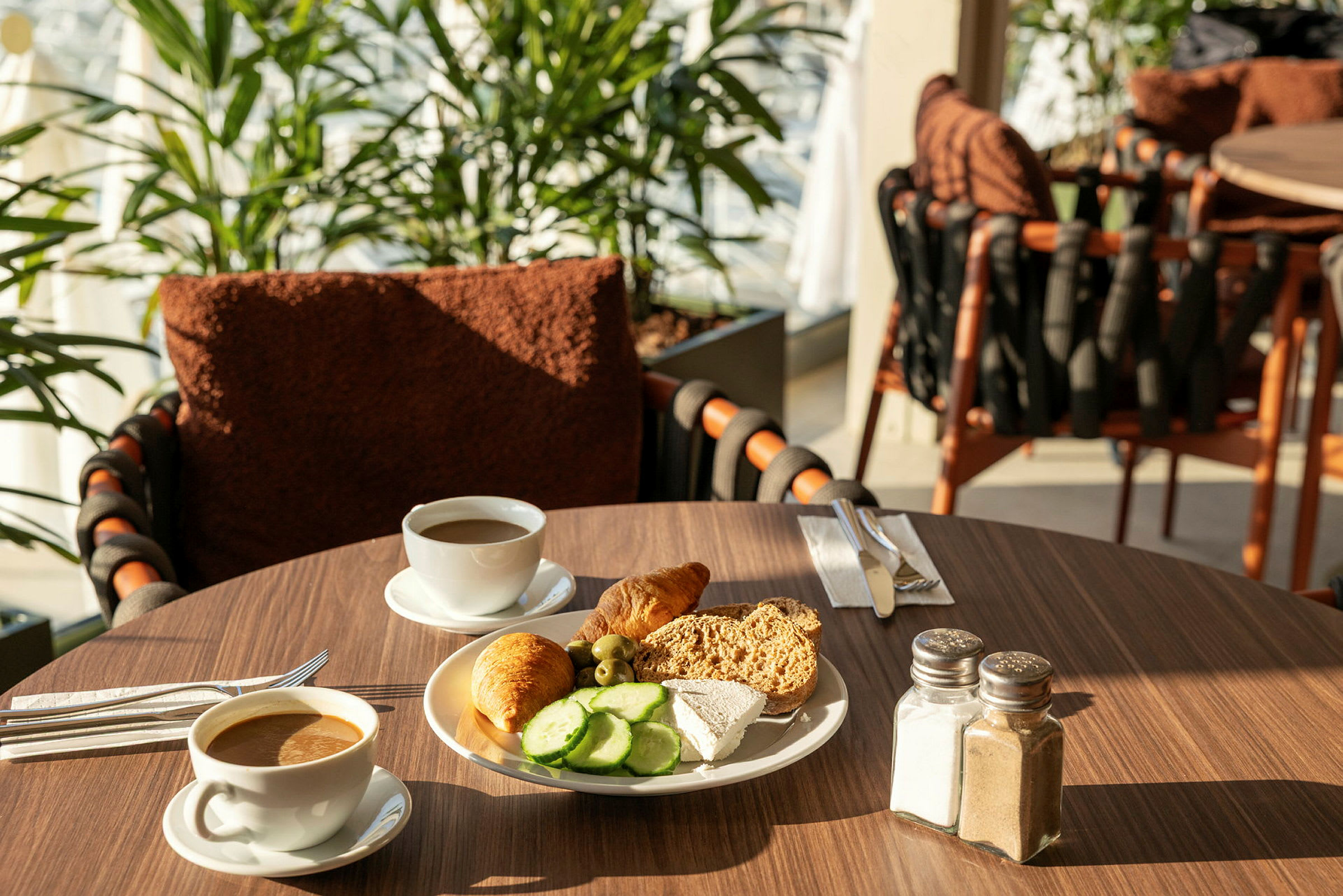 En frokostoppsats med kaffe og en tallerken med brød, ost, agurkskiver og en croissant på et bord. (AI-generert tekst)