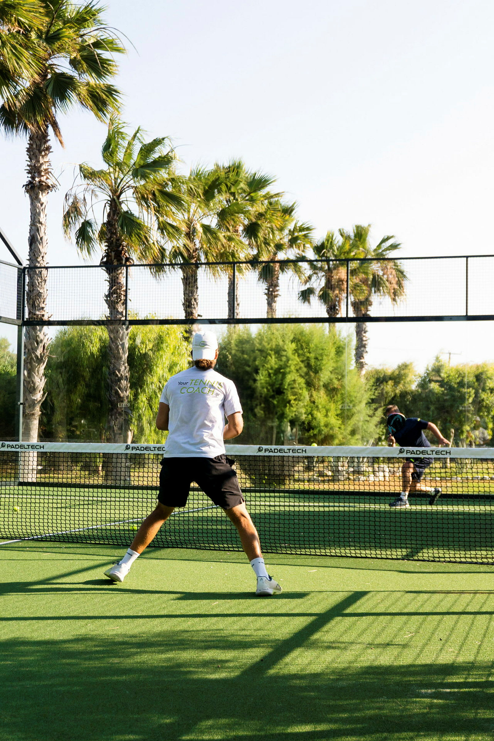 En mann spiller padeltennis på en utendørsbane med palmer rundt. (AI-generert tekst)