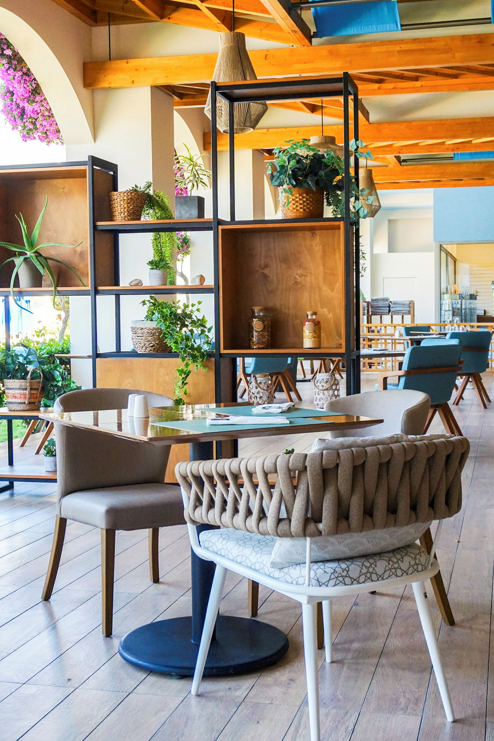 Bilde av en elegant innredet kafé eller restaurant, med moderne møbler, tredetaljer og dekorasjoner i form av grønne planter. (AI-generert tekst)