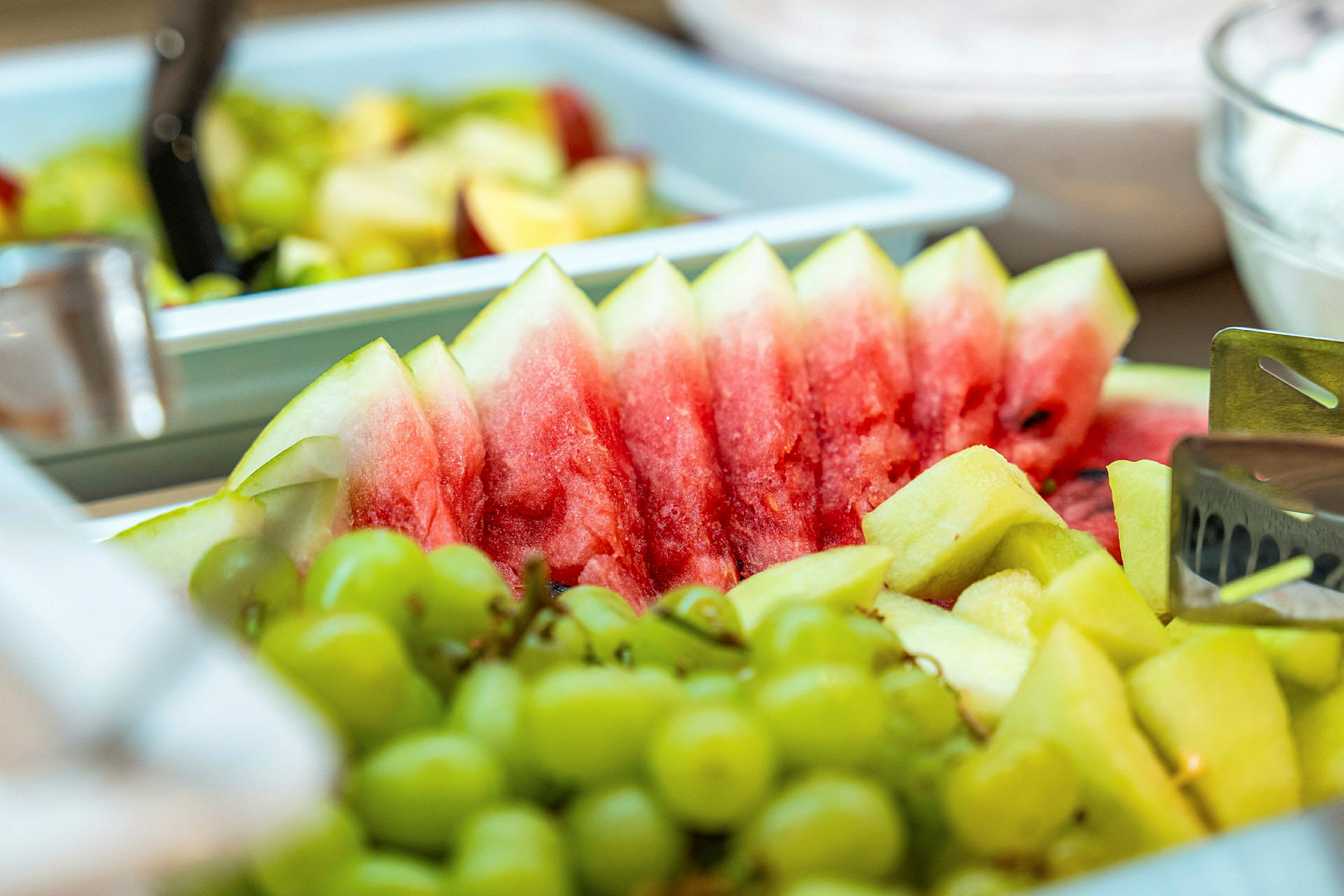 Stykker av fersk vannmelon, druer og ananas ligger på et serveringsfat. (AI-generert tekst)