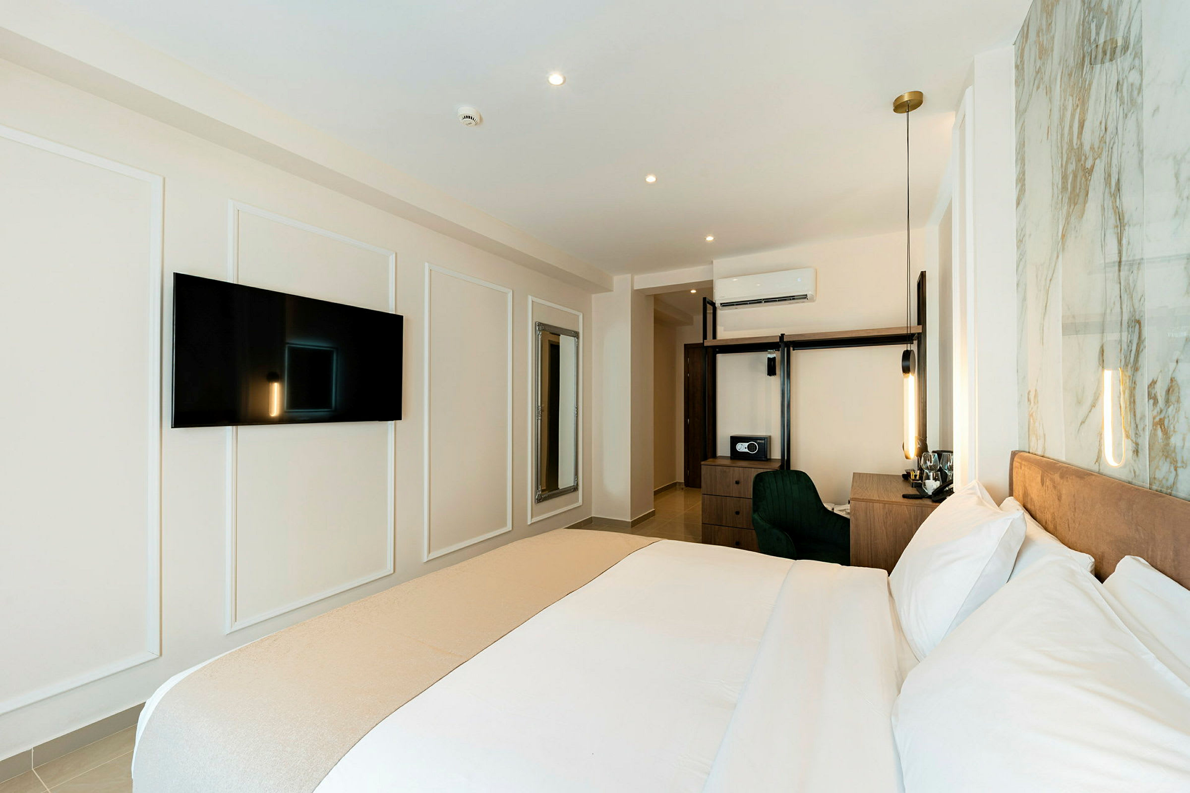 Et moderne hotellrom med en stor seng, TV på veggen, skrivebord og oppbevaringsmøbler. (AI-generert tekst)