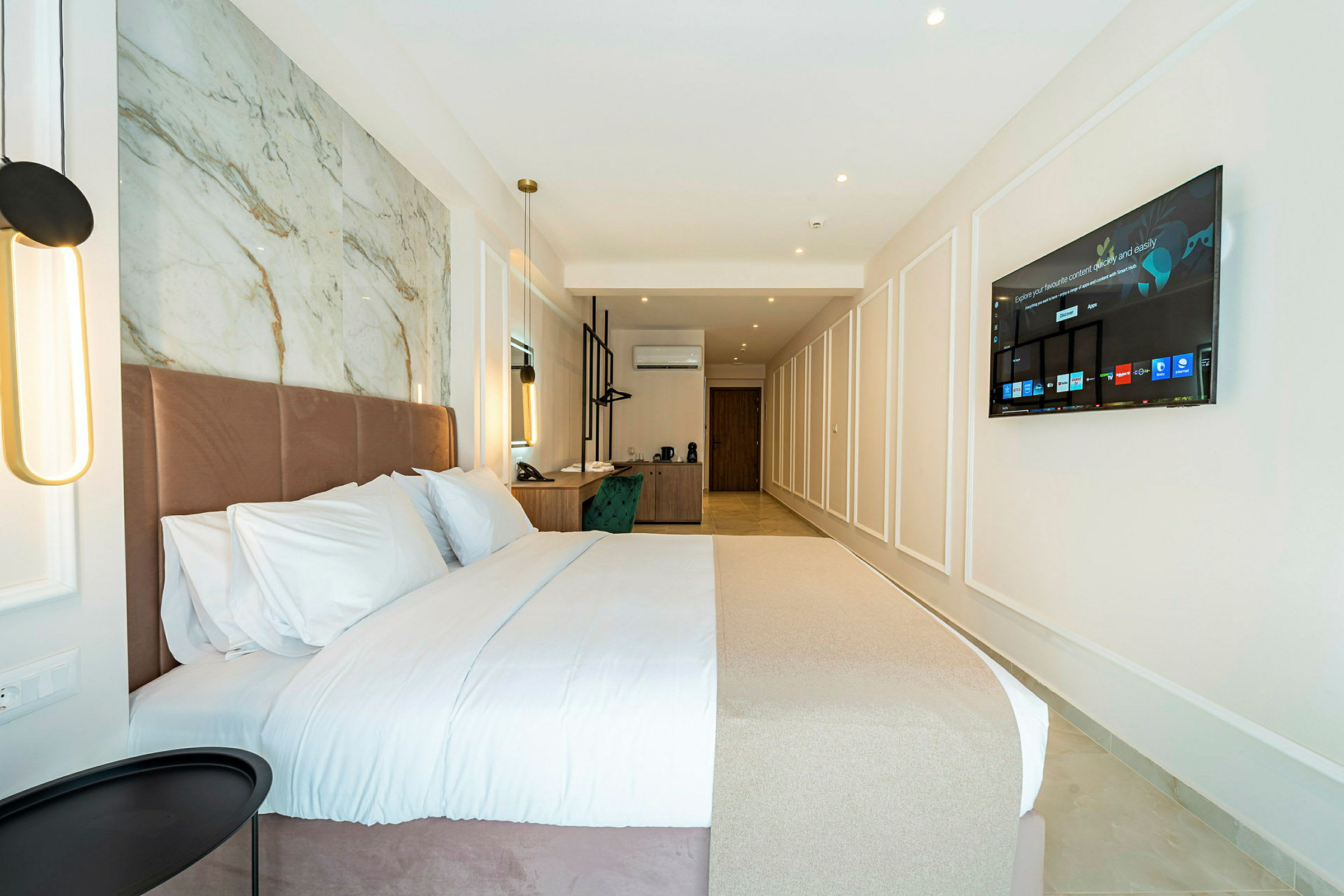 Hotellrom med en stor seng, skrivebord og veggmontert TV. (AI-generert tekst)