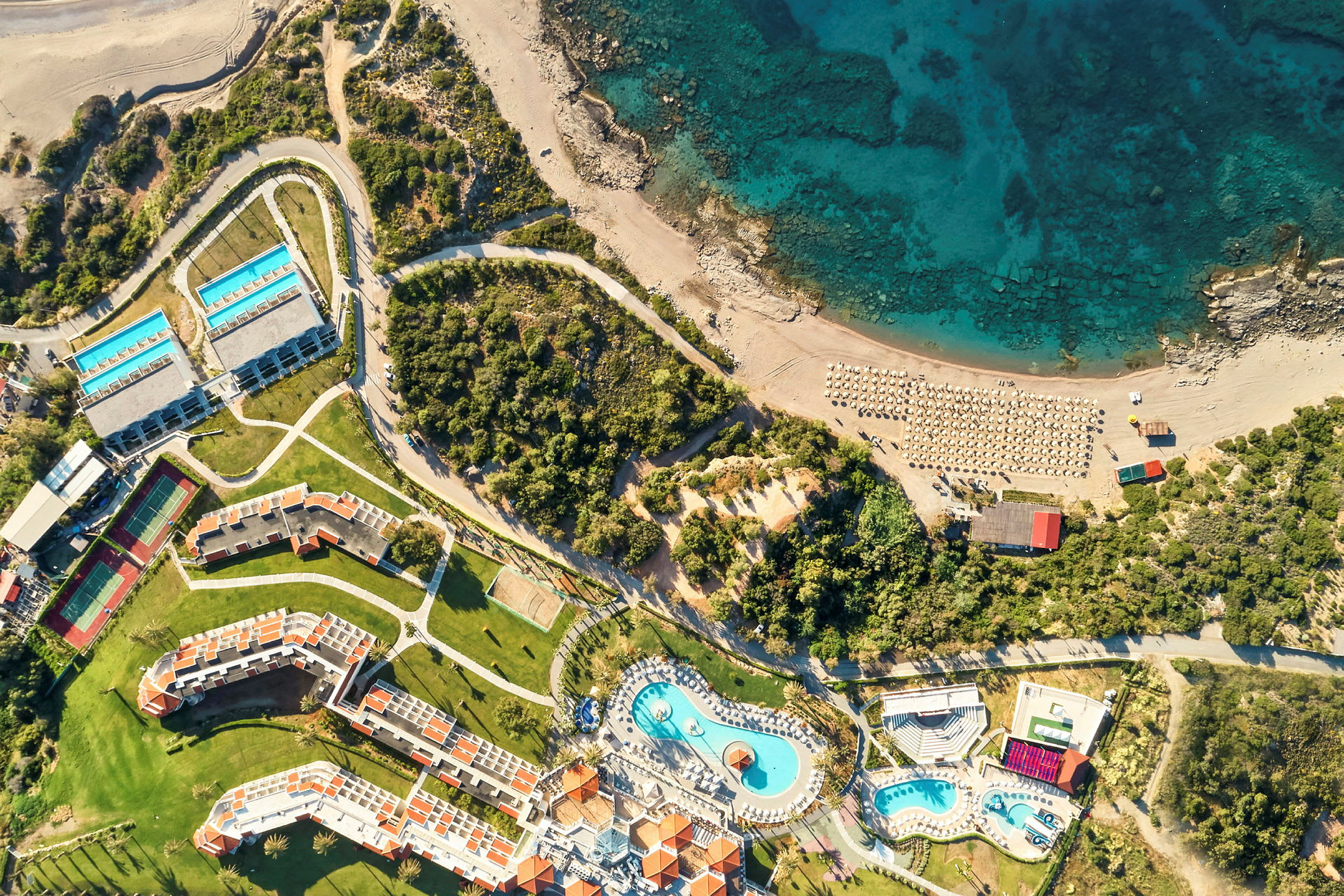 Luftfoto av et hotellområde med bassenger, bygninger, strand og hav. (AI-generert tekst)