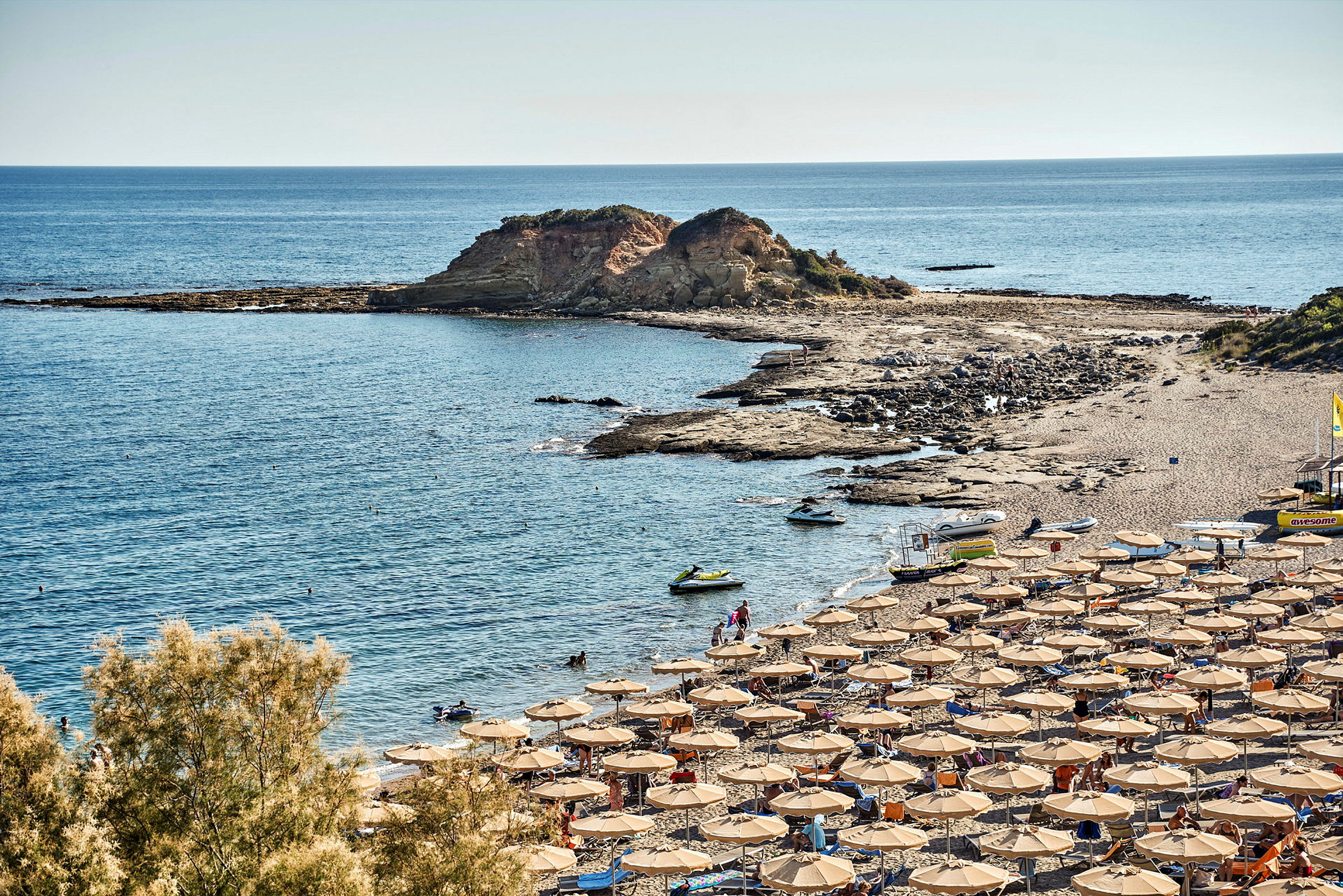 Solstoler og parasoller på en strand ved kysten med klipper og hav. (AI-generert tekst)