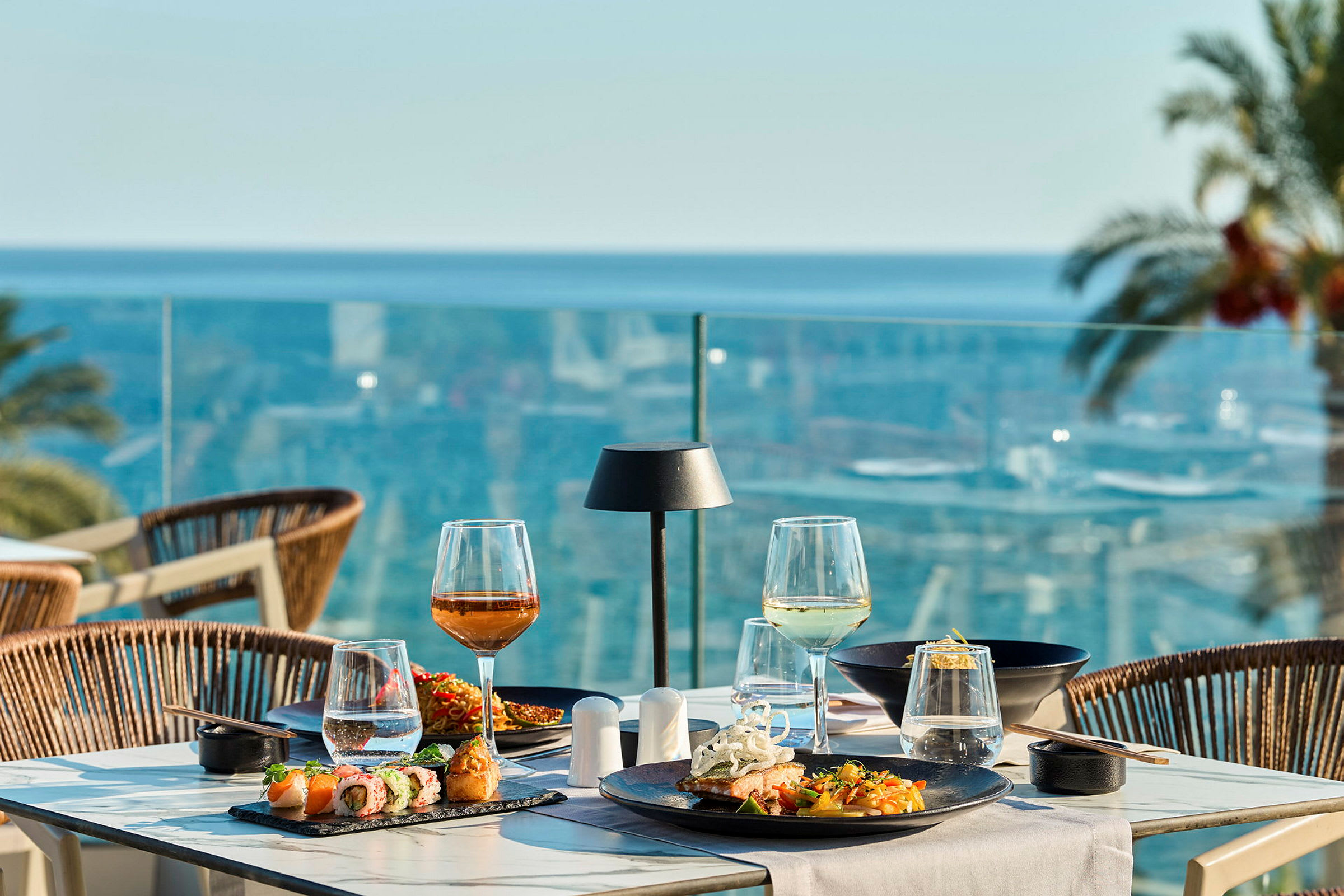 Et dekket bord med mat og drikke på en terrasse med utsikt over havet. (AI-generert tekst)
