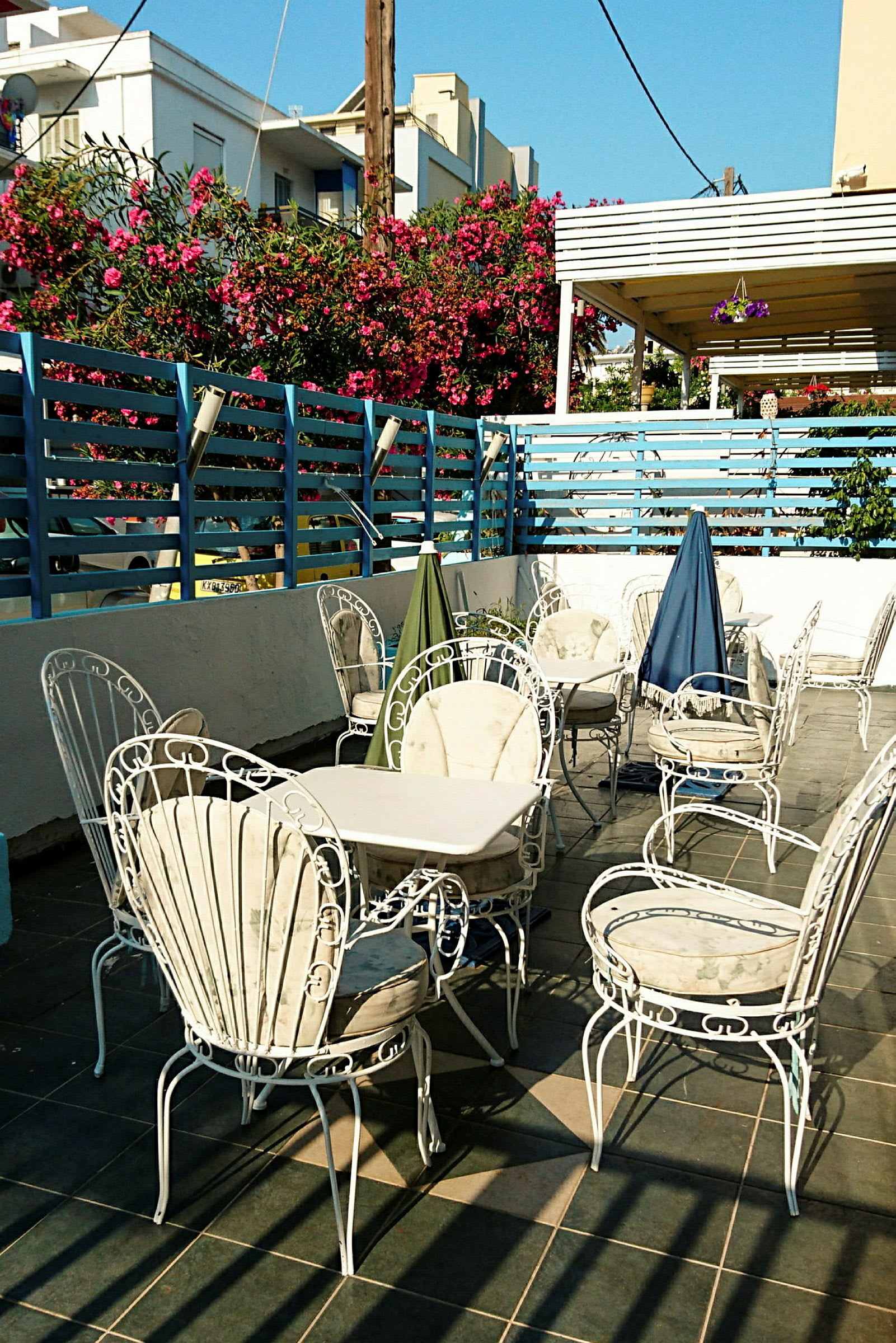 En terrasse med hvite hagemøbler og bord, omgitt av et blåmalt gjerde og blomstrende busker. (AI-generert tekst)