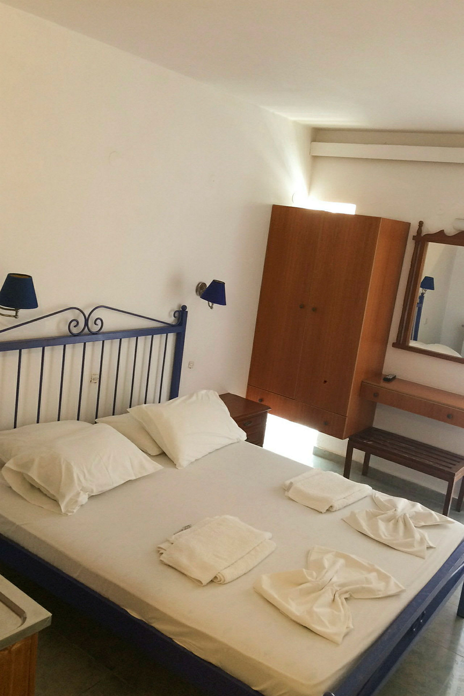 Et hotellrom med en seng med hvitt sengetøy, håndklær arrangert på sengen og møbler som inkluderer garderobe og speil. (AI-generert tekst)