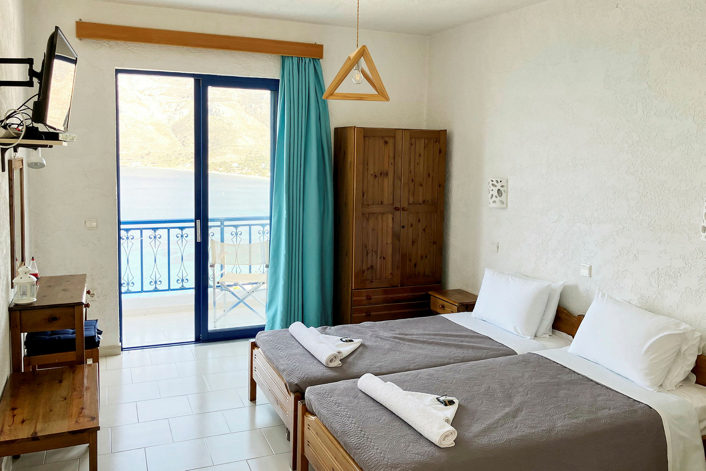 Et hotellrom med to enkeltsenger og utsikt over havet gjennom glassdører. (AI-generert tekst)
