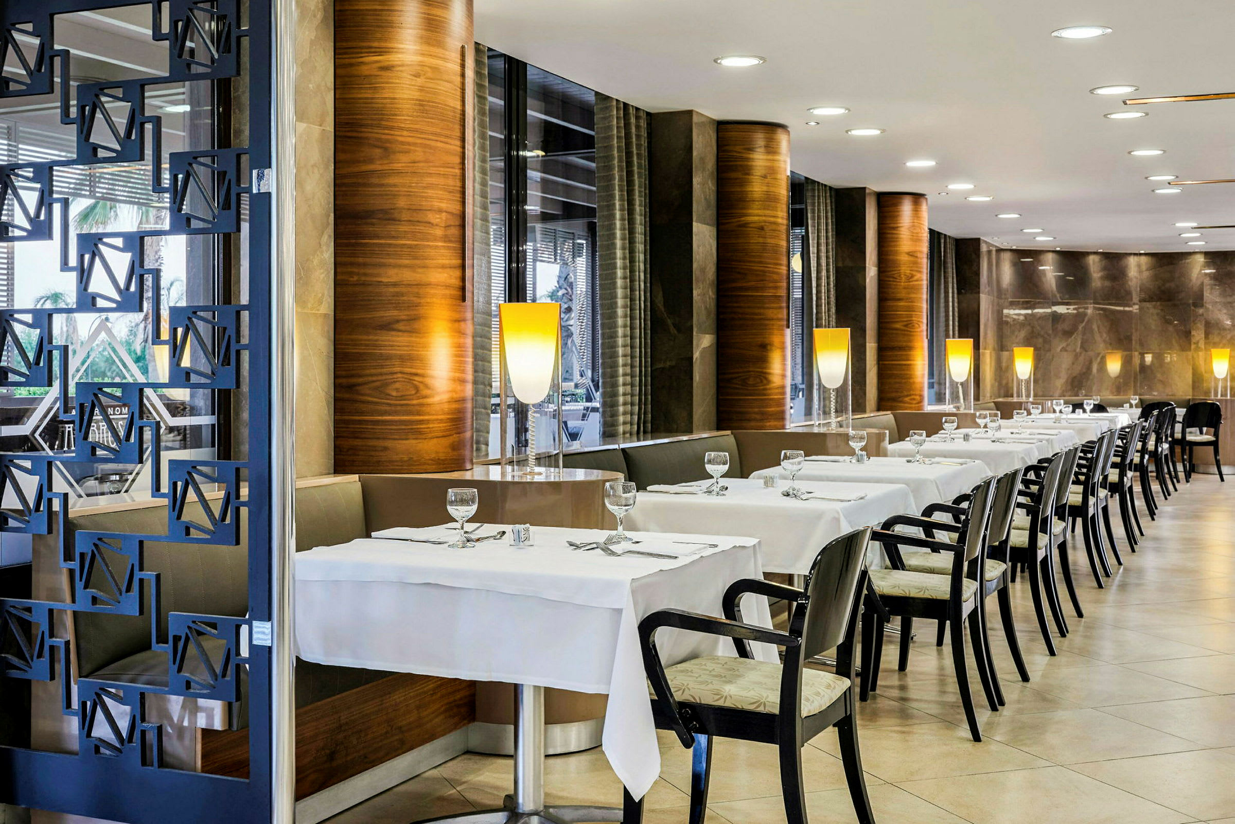 Interiør av en restaurant med dekkede bord og stoler. (AI-generert tekst)