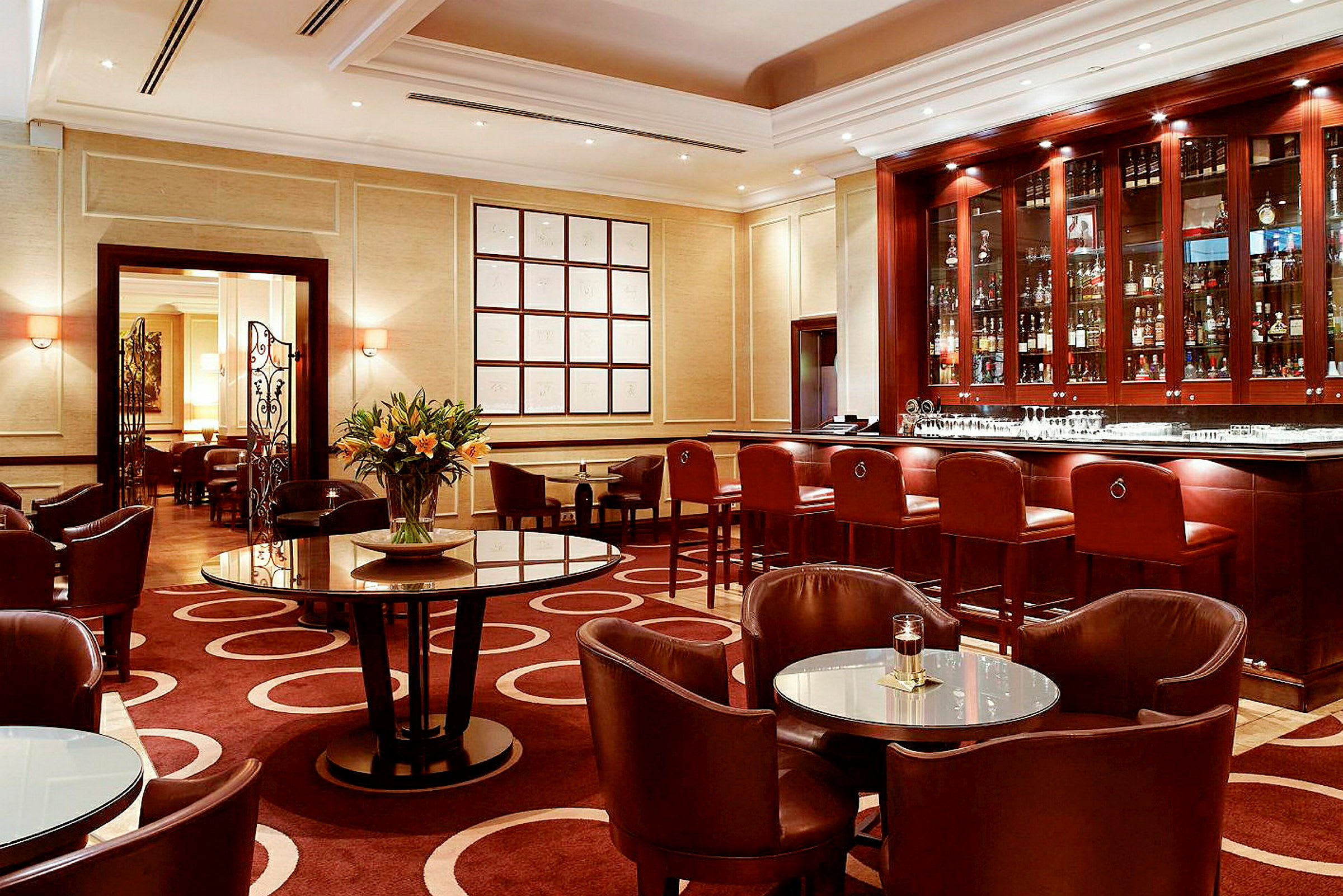 En elegant hotellbar med mørke trematerialer, flere bord og stoler samt en blomst i midten. (AI-generert tekst)