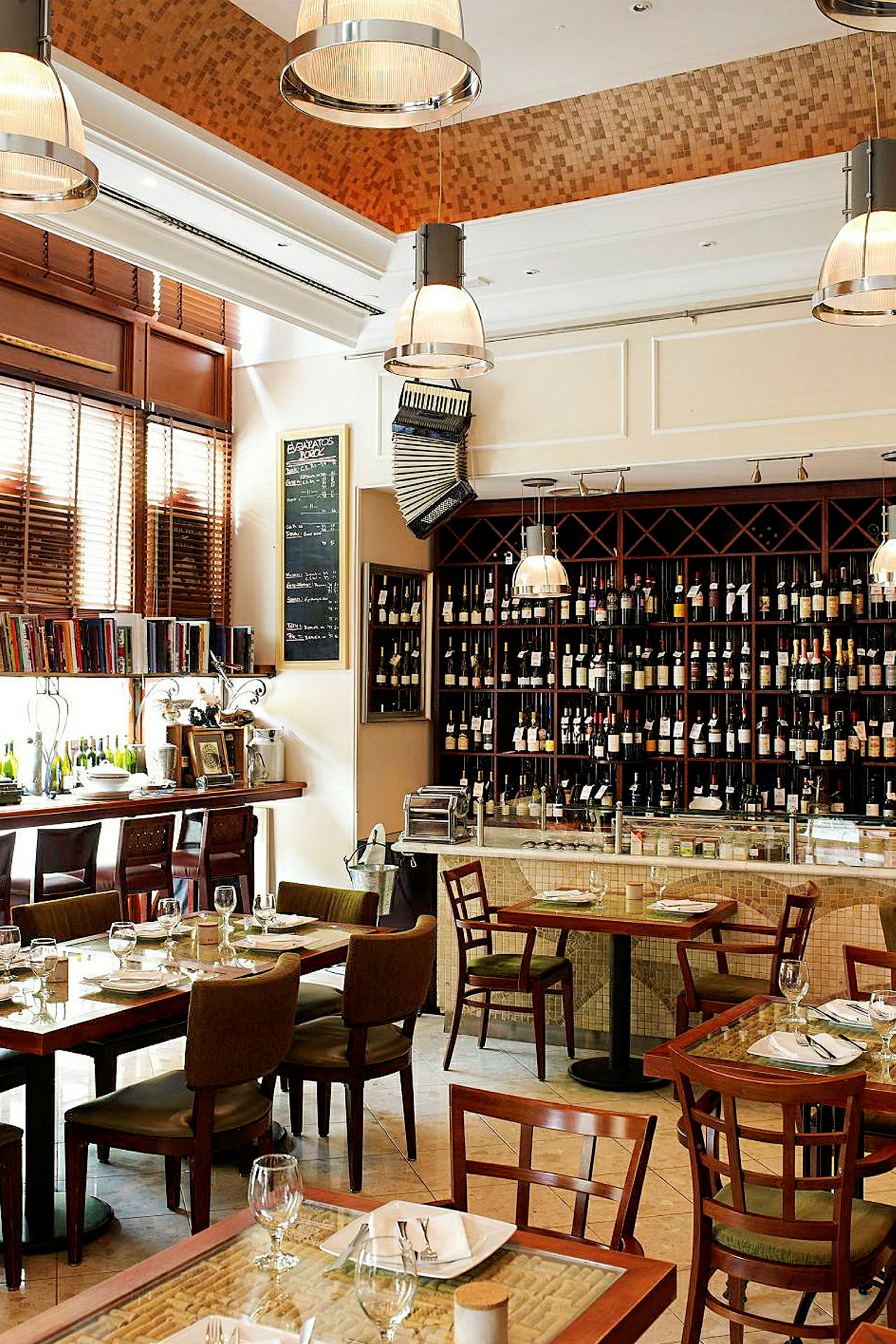 Interiør av en restaurant med spisebord og stoler, en hylle med vinflasker og en bardisk. (AI-generert tekst)